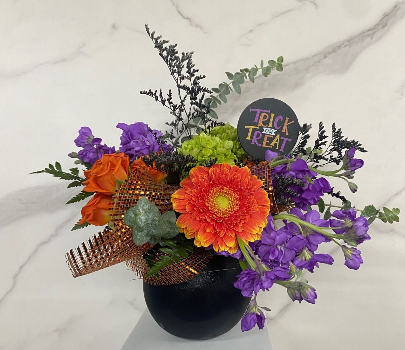 Orange and purple floral arrangement in a black vase with a Trick or Treat sign