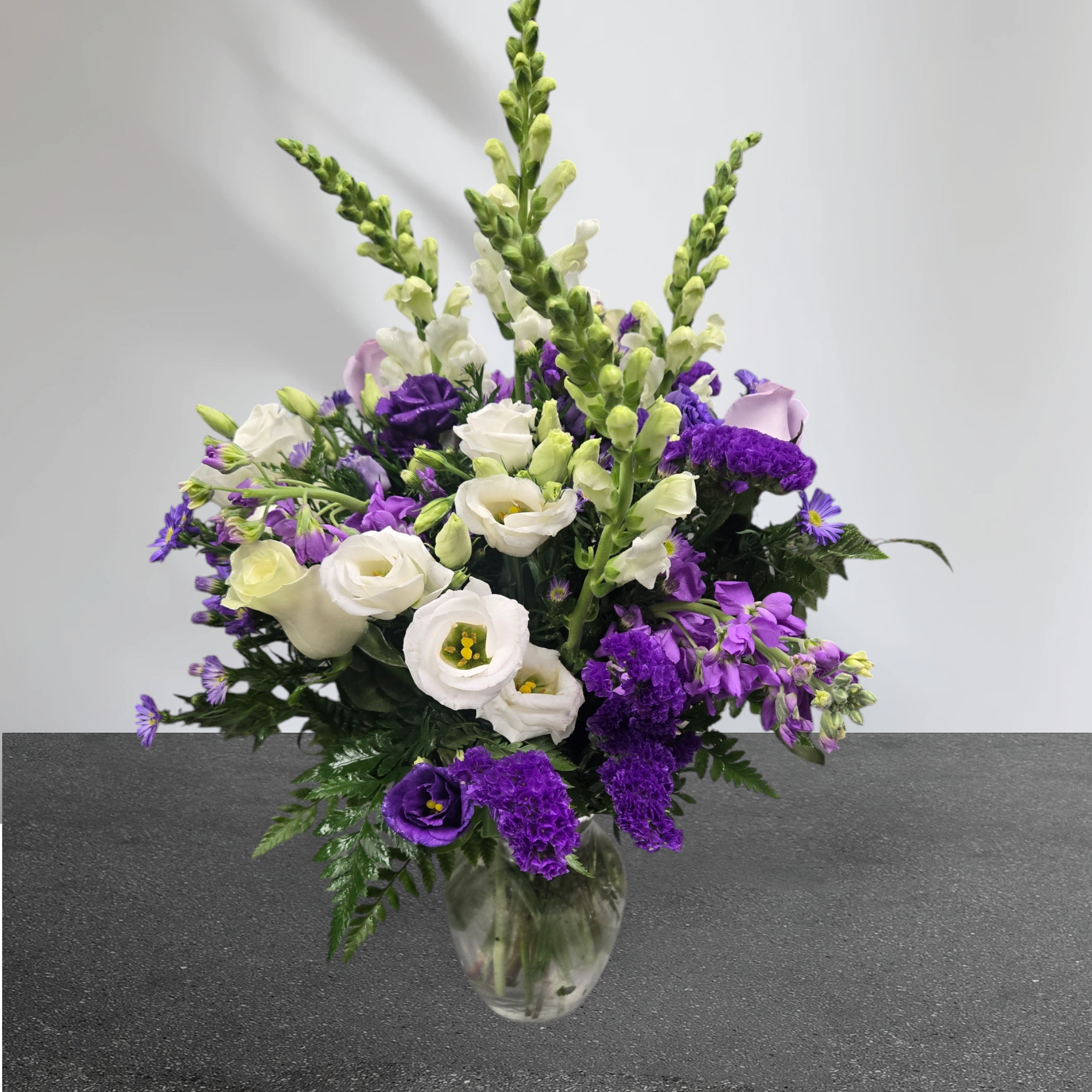 Tall arrangement of purple and white flowers in a clear glass vase