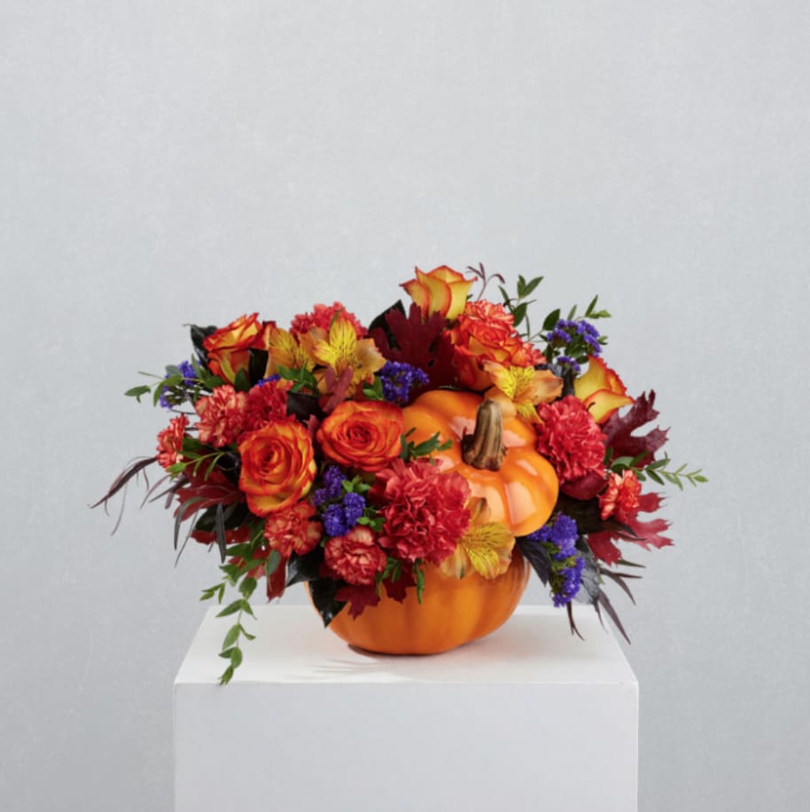 Autumn floral arrangement in a pumpkin container with orange and red blooms