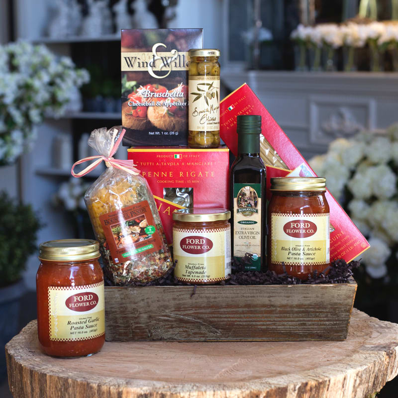 Italian-themed gourmet gift set with pasta, sauces, and olive oil arranged in a wooden tray.