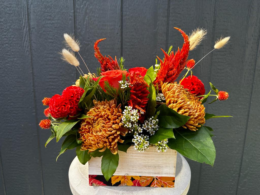 Red and orange floral arrangement in a wooden box with green leaves