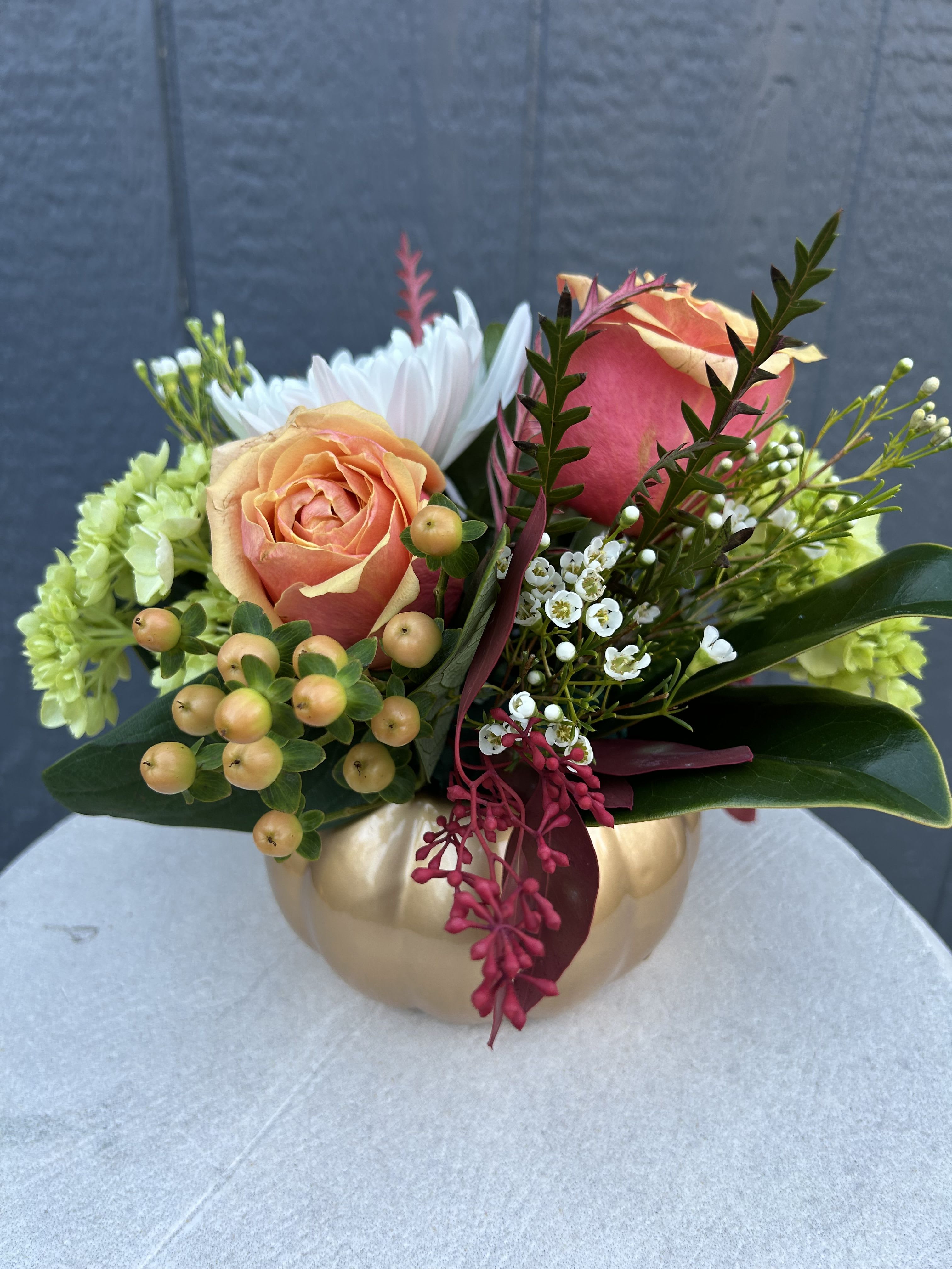 Peach and pink roses arranged in a gold pumpkin vase