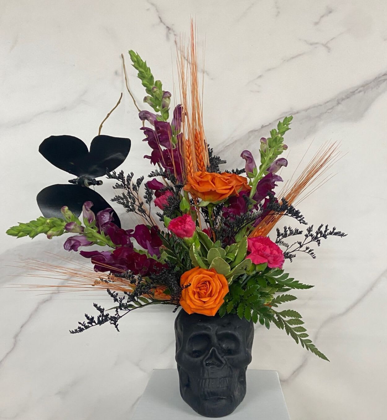 Orange and purple floral arrangement in a black skull vase