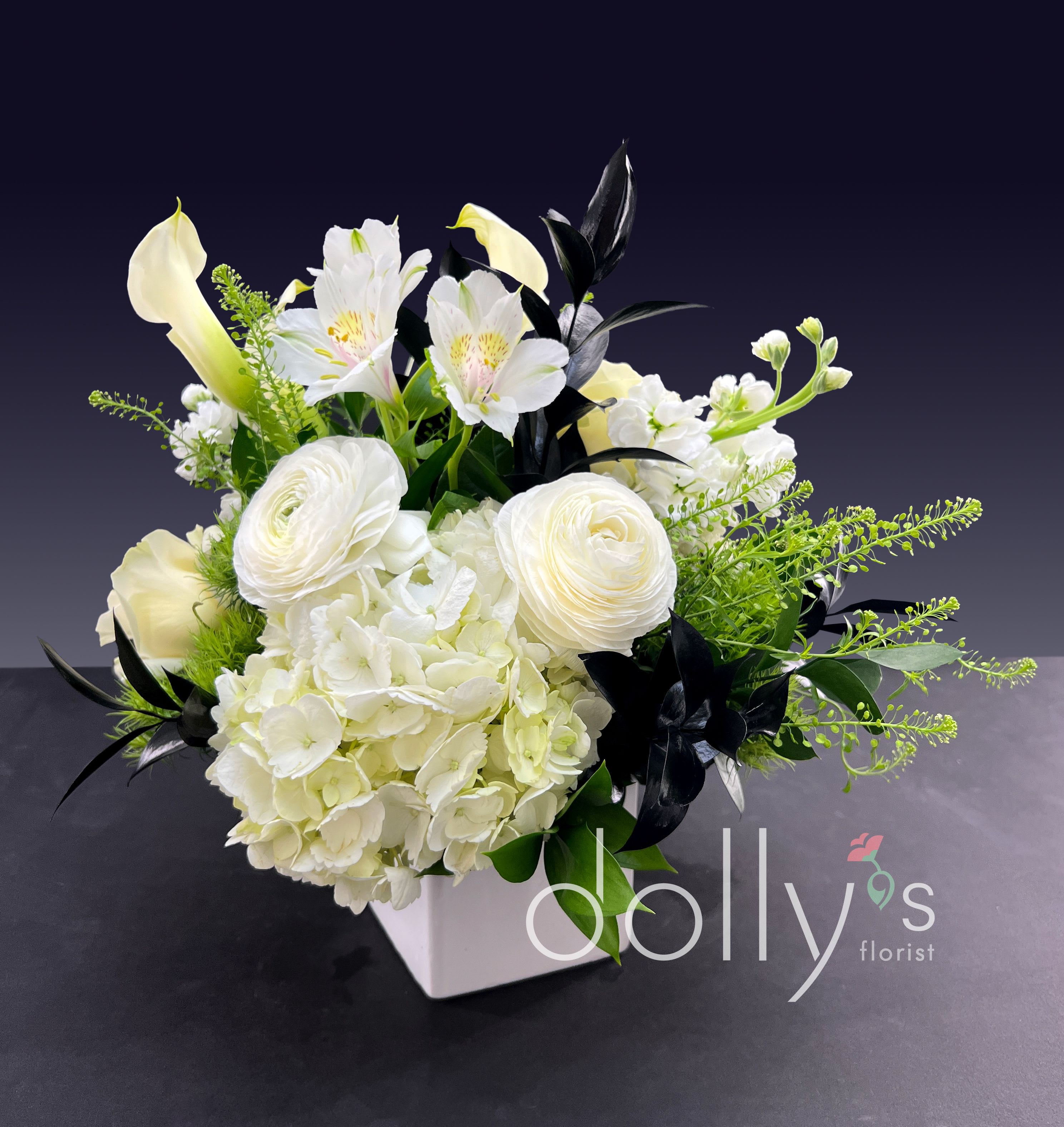 White floral arrangement in a square vase with calla lilies and hydrangeas