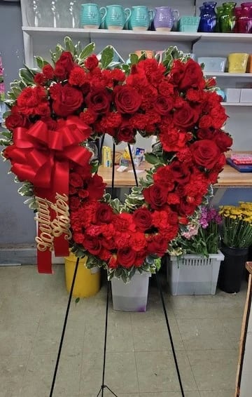 Heart-shaped red rose wreath on an easel with a large red bow