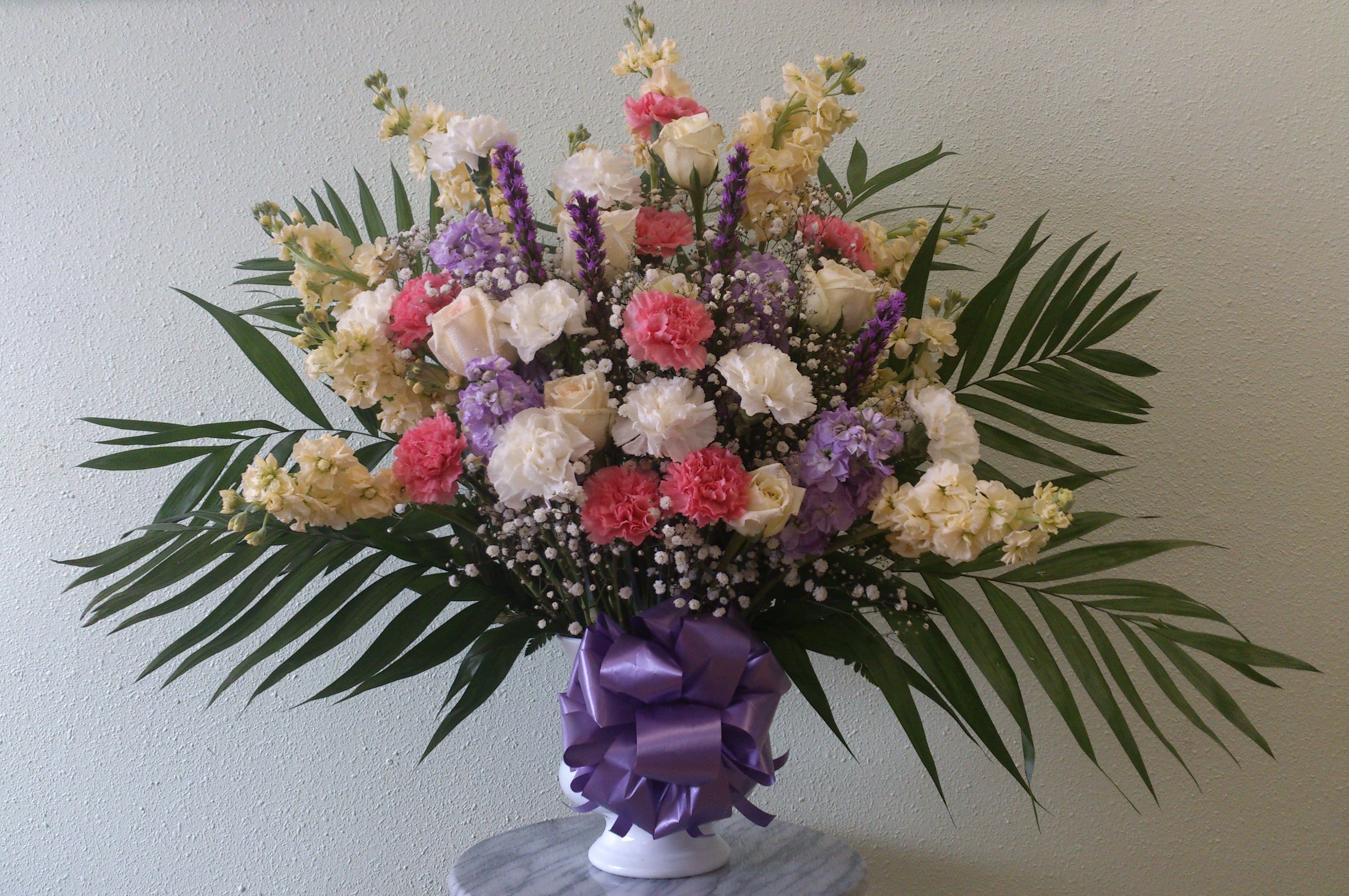 Mixed bouquet of carnations and roses in a white vase with a purple ribbon