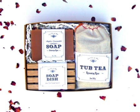 Gift box with soap, soap dish, and tub tea surrounded by rose petals