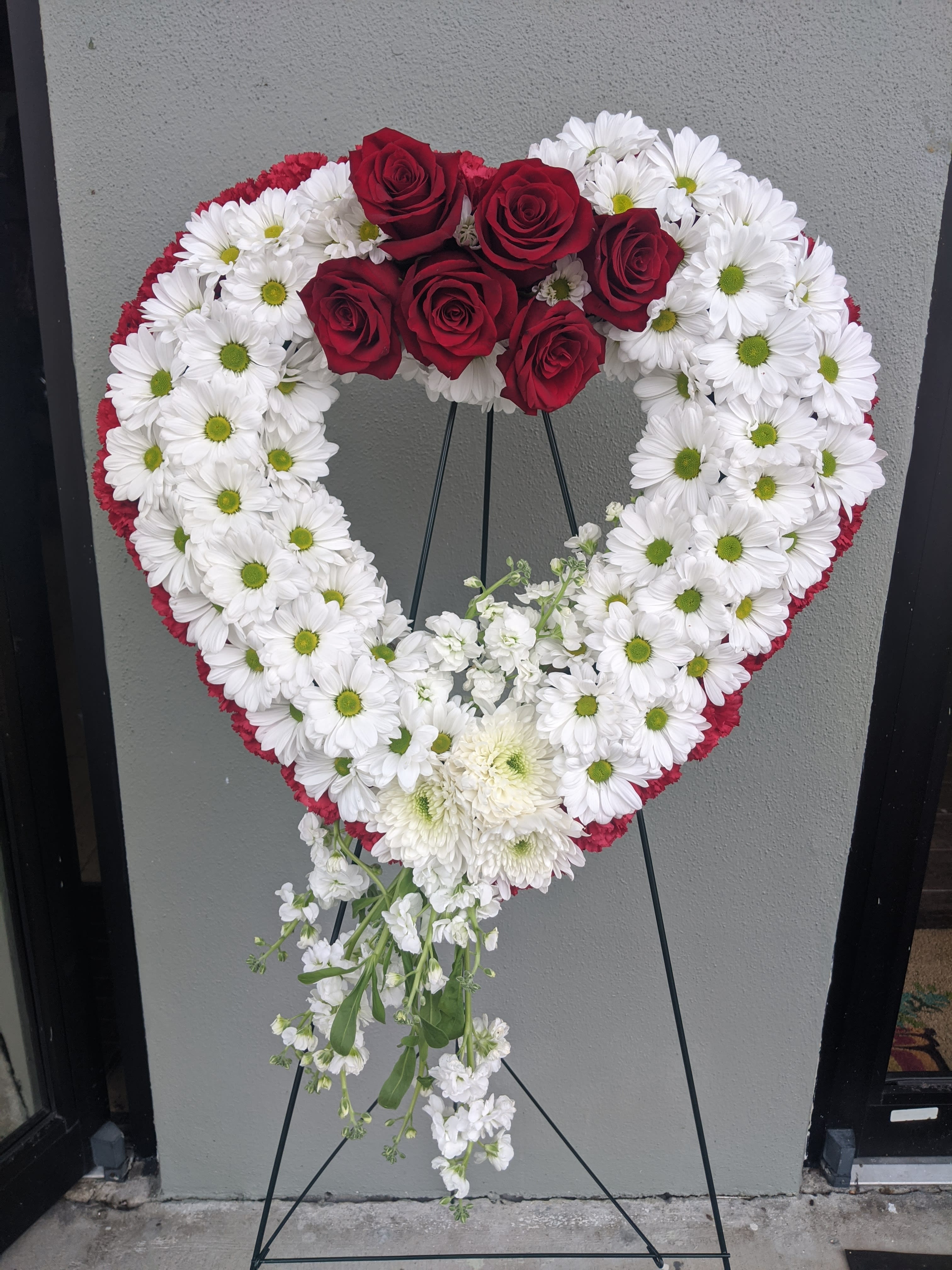 Heart-shaped floral wreath with red roses and white daisies on a stand