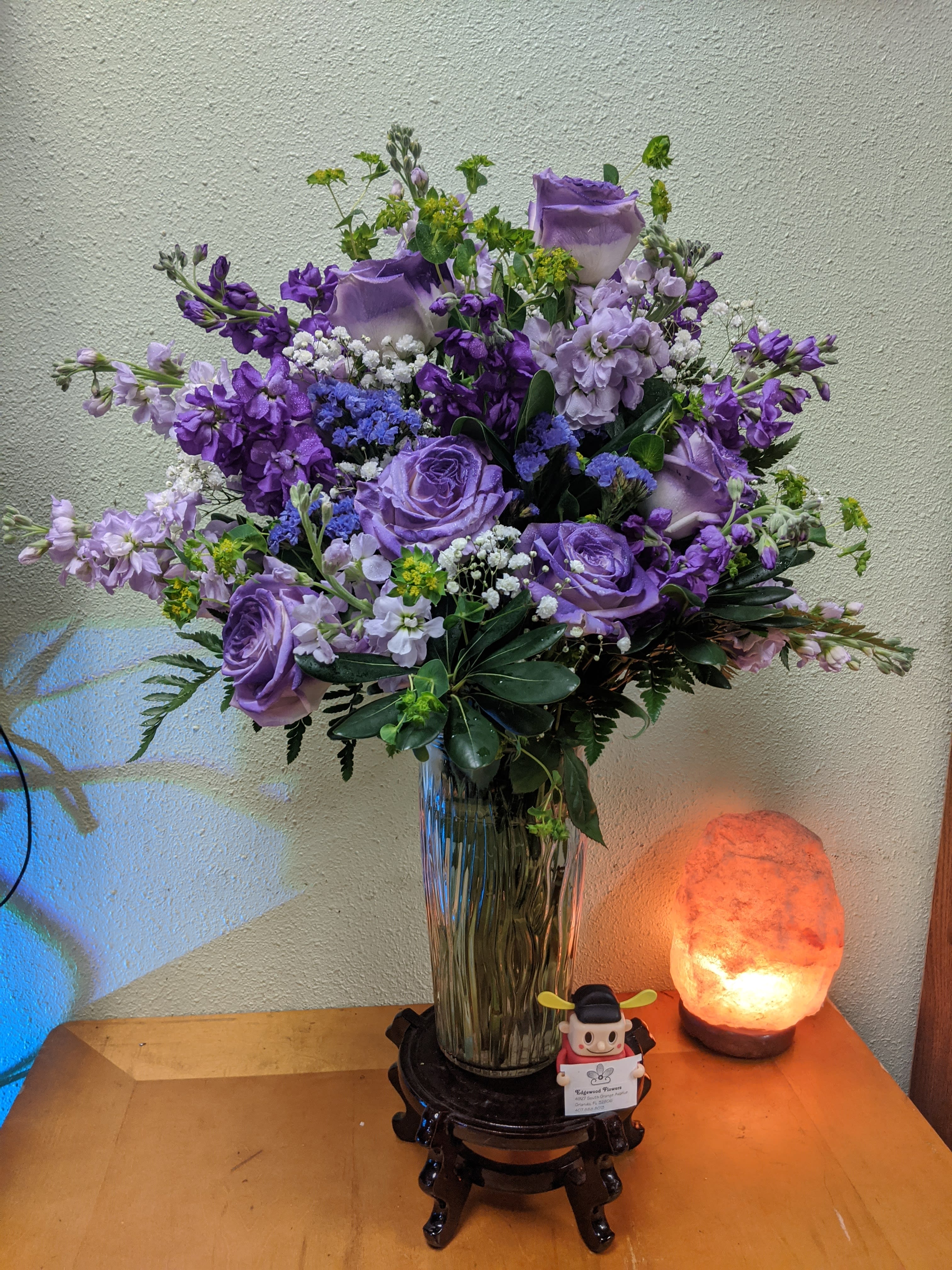 Purple floral arrangement in a glass vase on a small stand