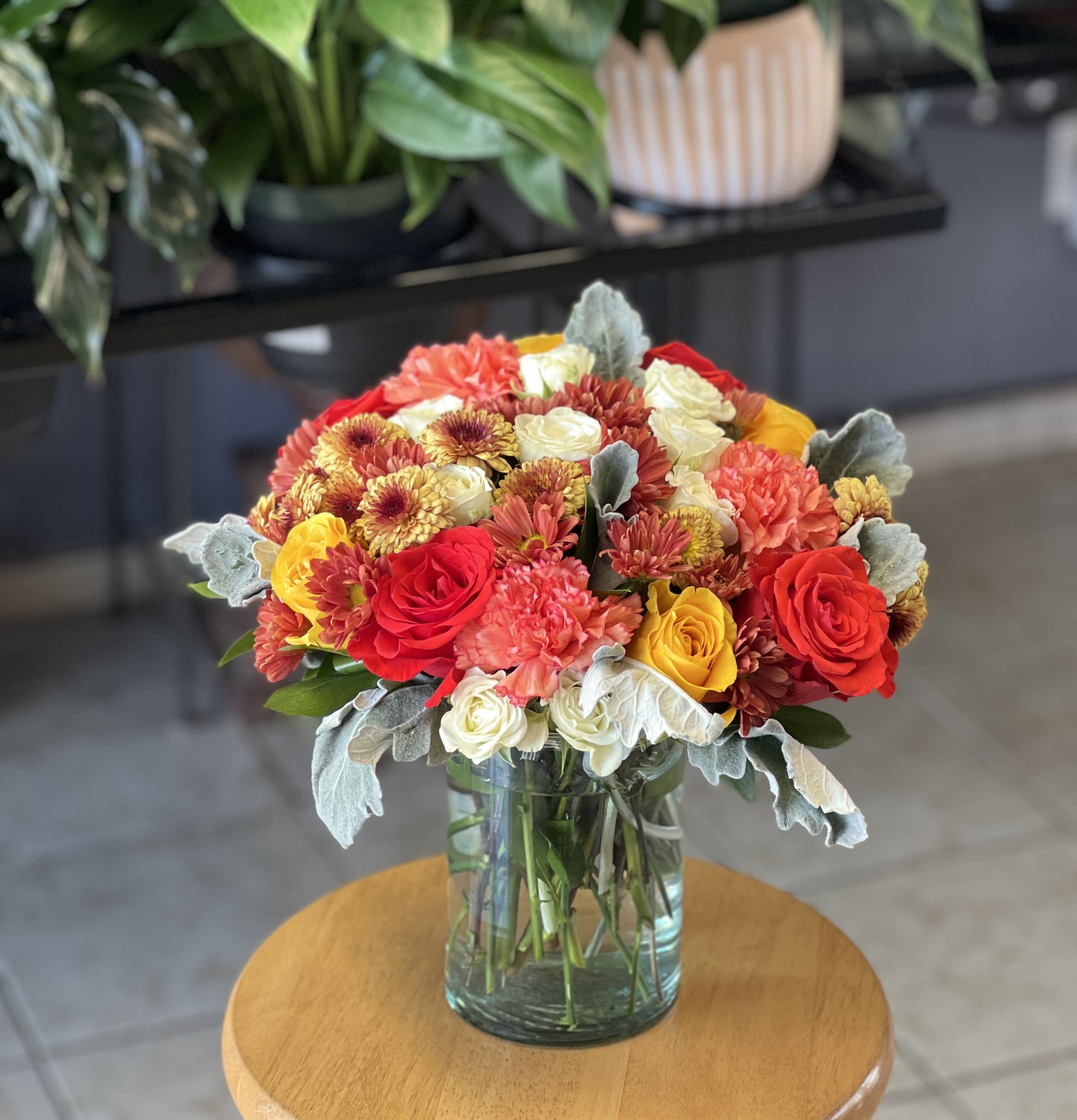 Mixed bouquet of red, yellow, white, and peach flowers in a glass vase