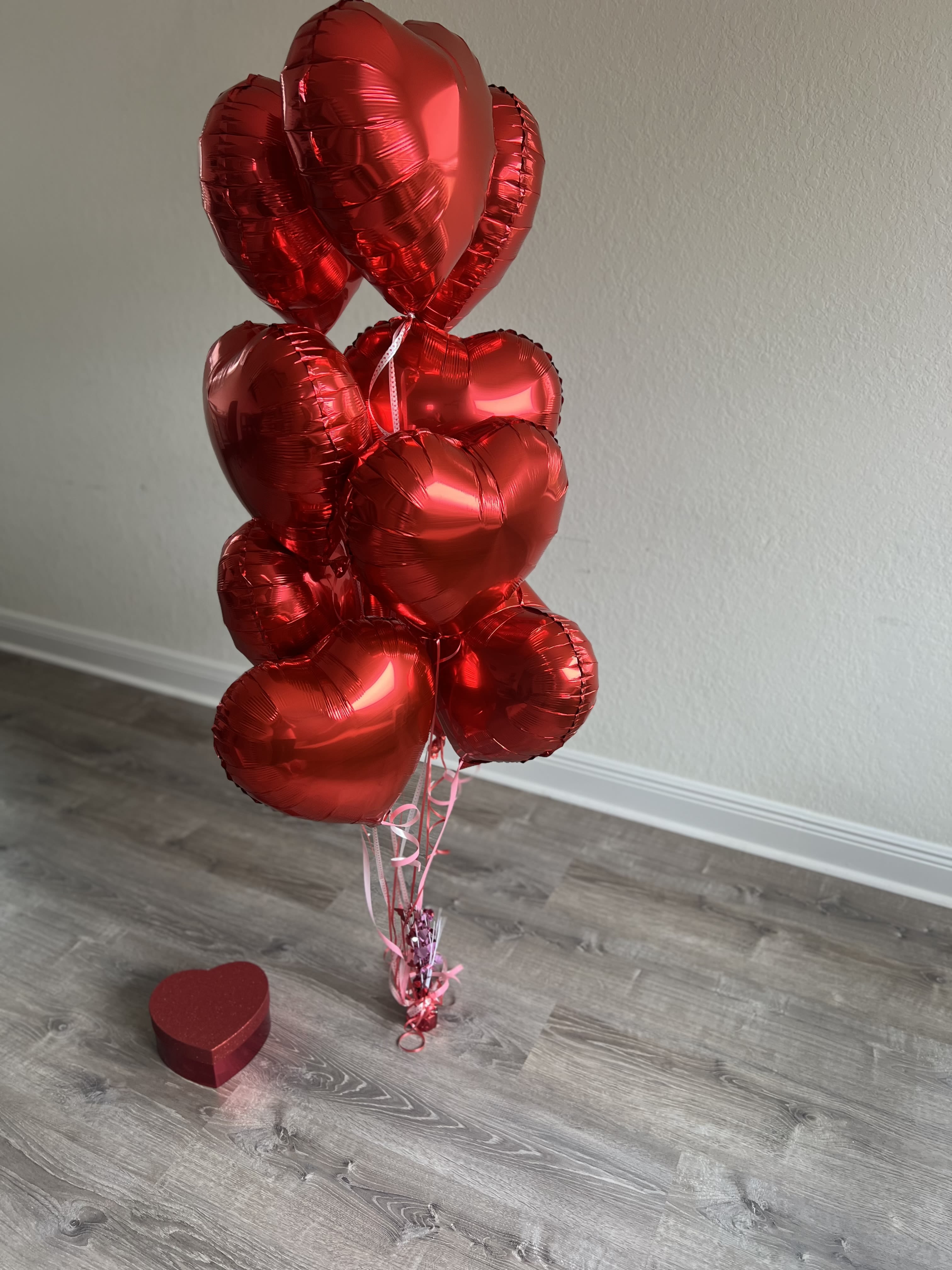 Cluster of red heart-shaped balloons with a small heart gift box on the floor