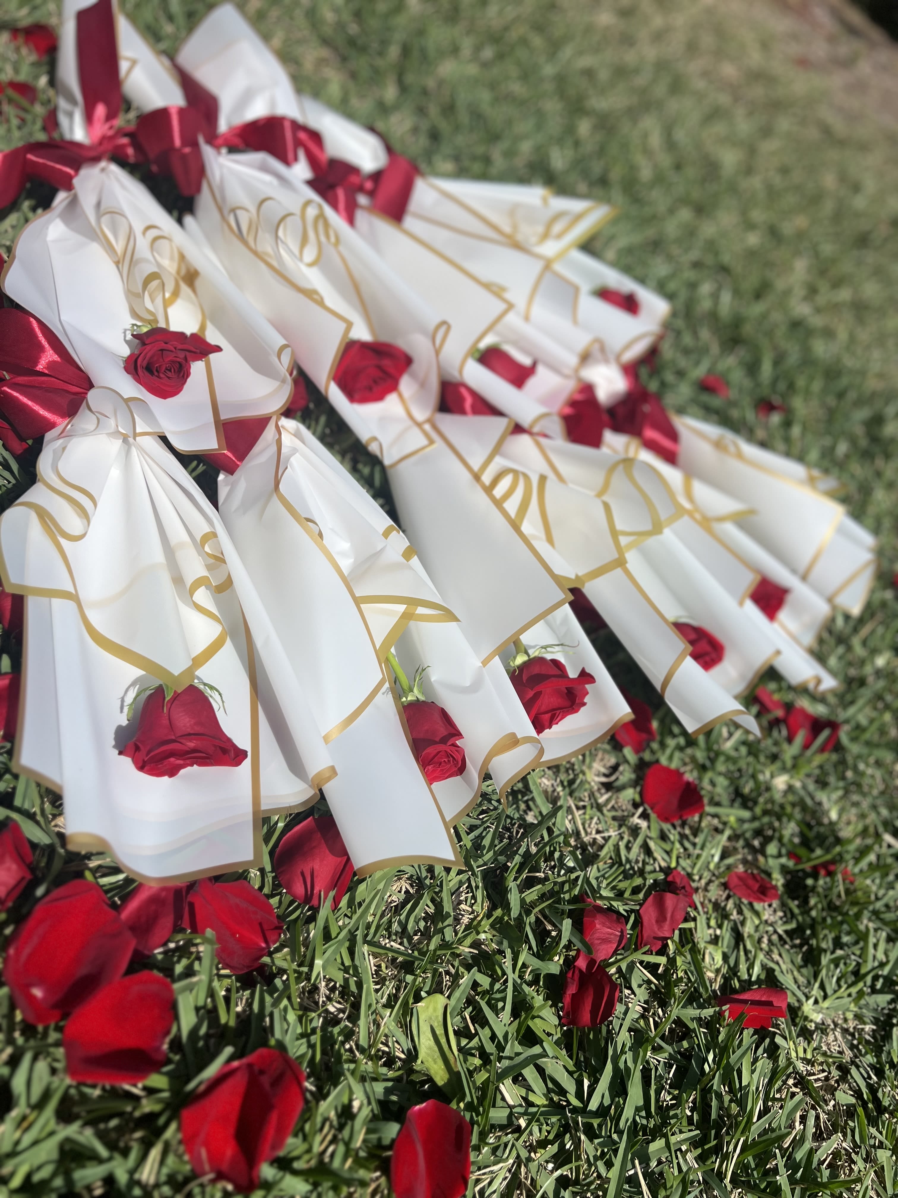 Red roses wrapped in white paper with gold trim and red ribbons on grass