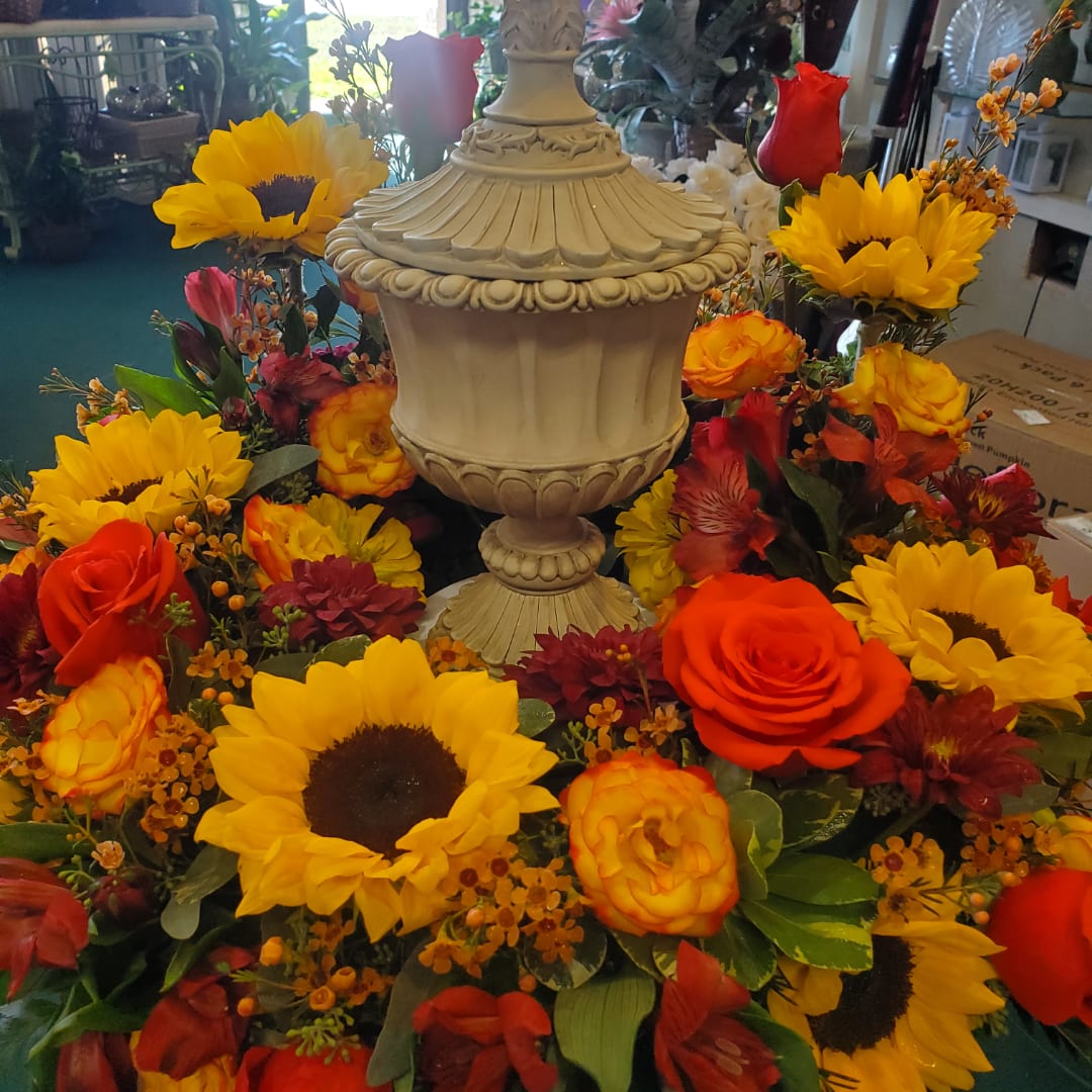 Colorful floral arrangement around an ornate cream urn with sunflowers and roses