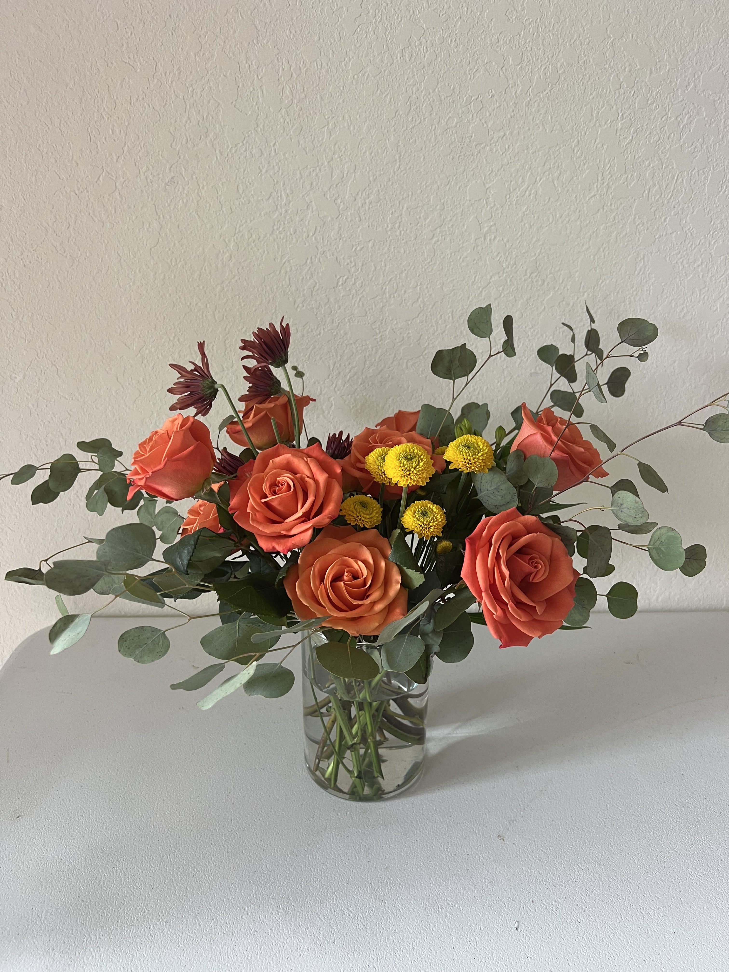 Orange roses and yellow button mums in a clear glass vase