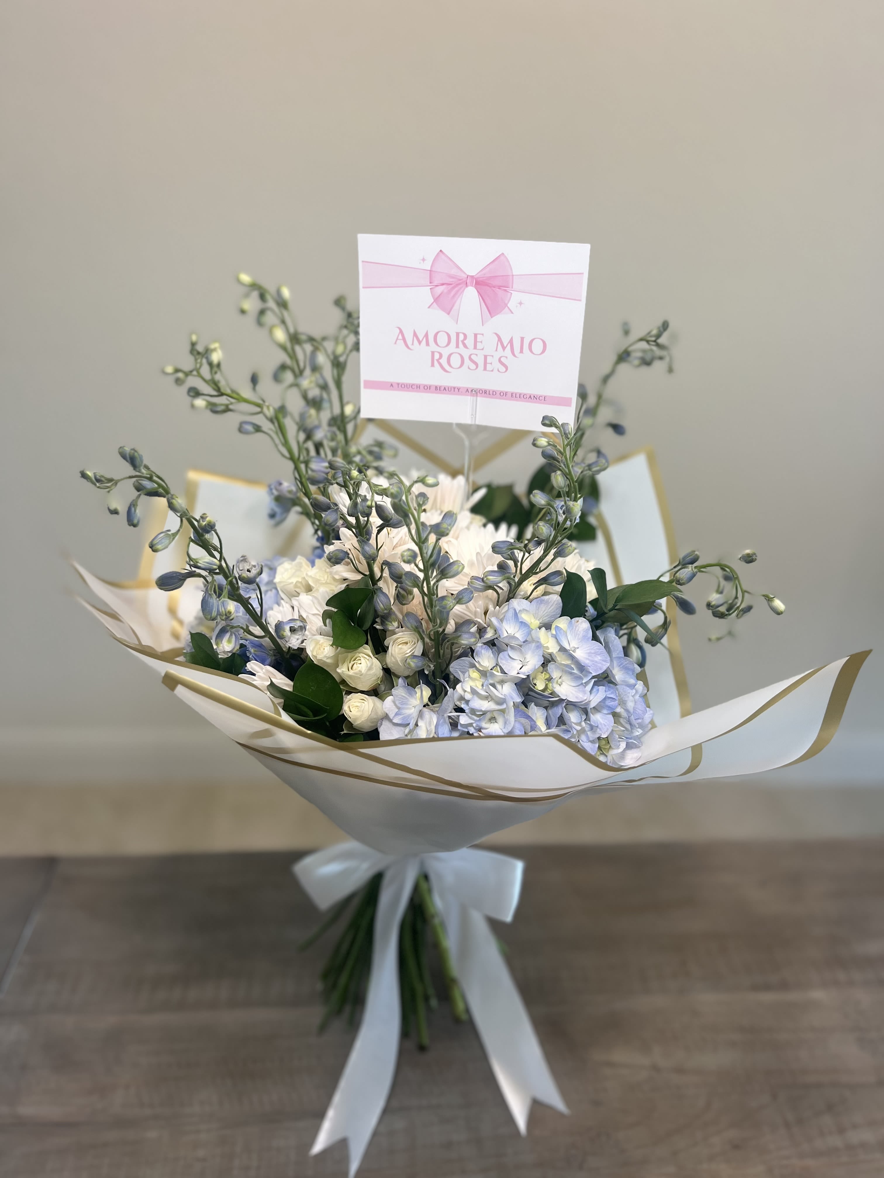 Bouquet of pale blue and white flowers wrapped in white paper with a ribbon