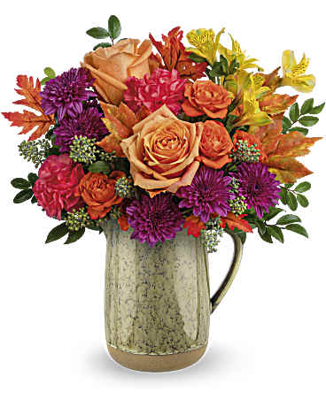 Teleflora's Harvest Joy Bouquet - Celebrate the essence of fall with this abundant bouquet of autumnal roses, artfully arranged in a rustic glazed ceramic pitcher. The Harvest Joy Bouquet features peach roses, vibrant orange spray roses, sunny yellow alstroemeria, and orange carnations. Accented with purple cushion spray chrysanthemums, seeded eucalyptus, huckleberry, and preserved oak leaves, presented in the Majestic Meadow Pitcher for a festive fall arrangement.