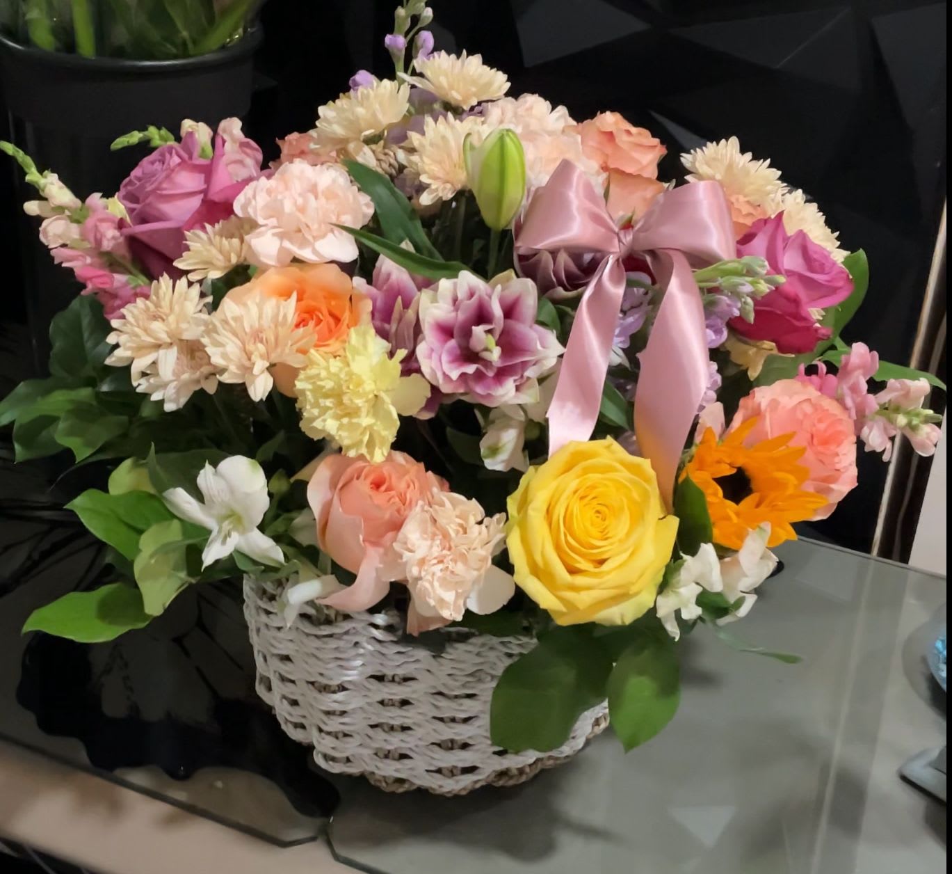 Mixed flower arrangement in a white wicker basket with a pink ribbon