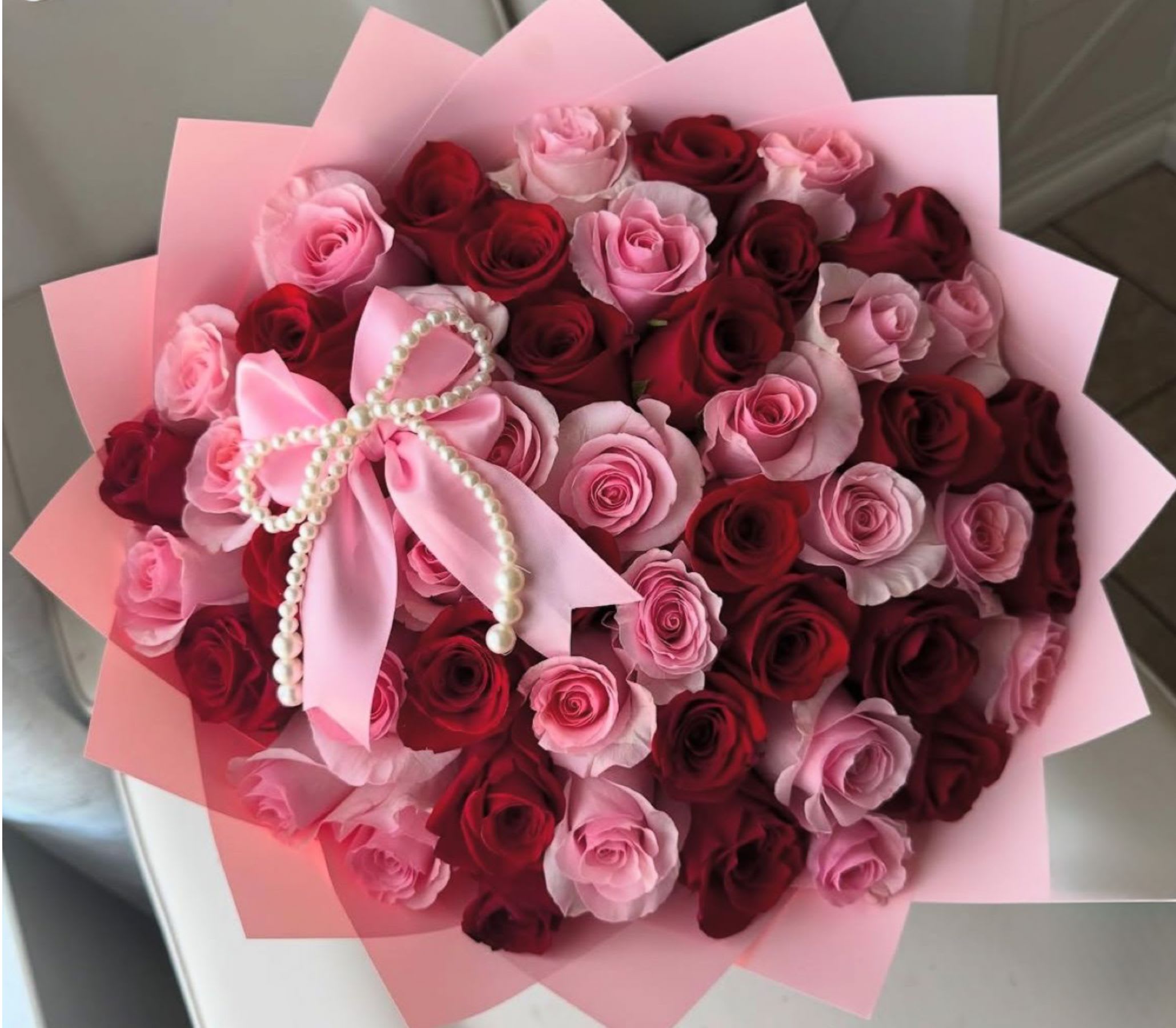 Bouquet of pink and red roses wrapped in pink paper with a pearl bow