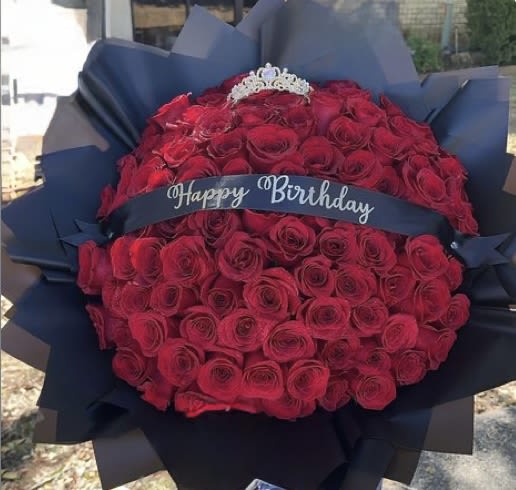 Bouquet of red roses wrapped in dark paper with a birthday ribbon