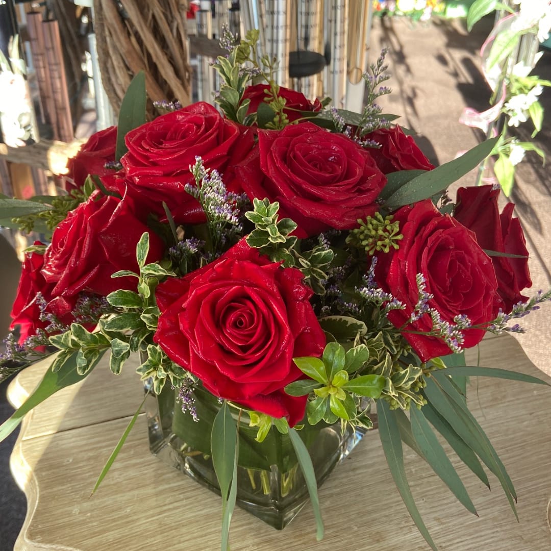 Red roses arranged in a clear square vase with mixed greenery