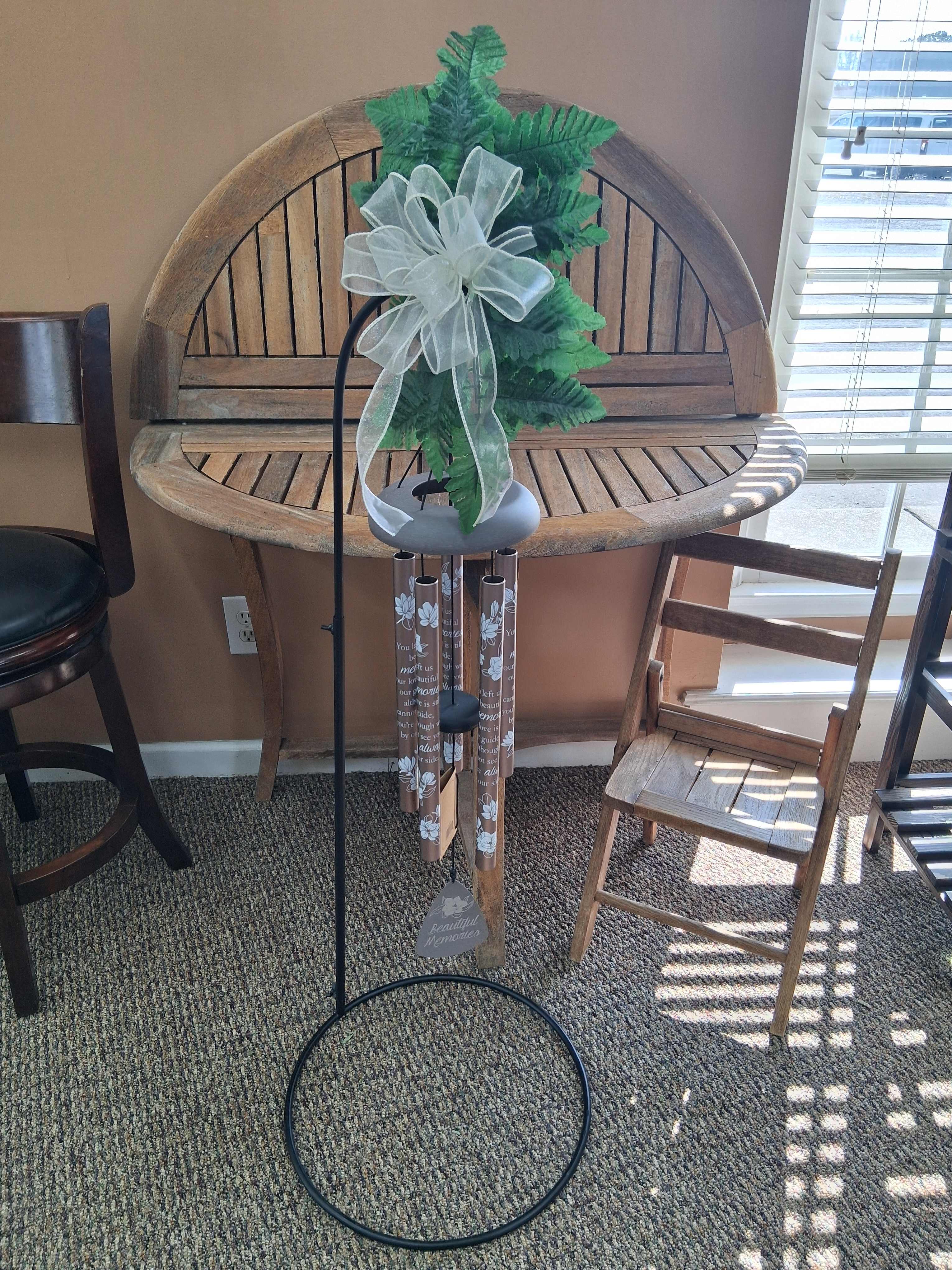 Memorial wind chime with faux greenery and a white bow on a metal stand