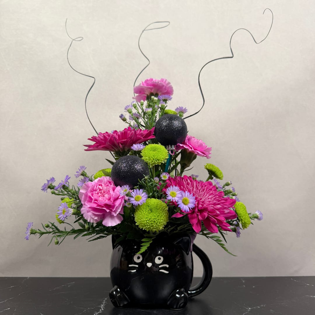 Pink and purple flower arrangement in a black cat mug with curly wire accents