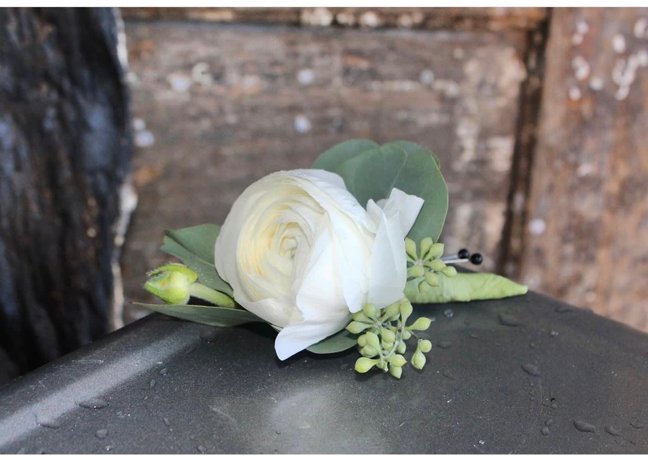 Small white ranunculus floral accent with berries and buds on a wet metal surface
