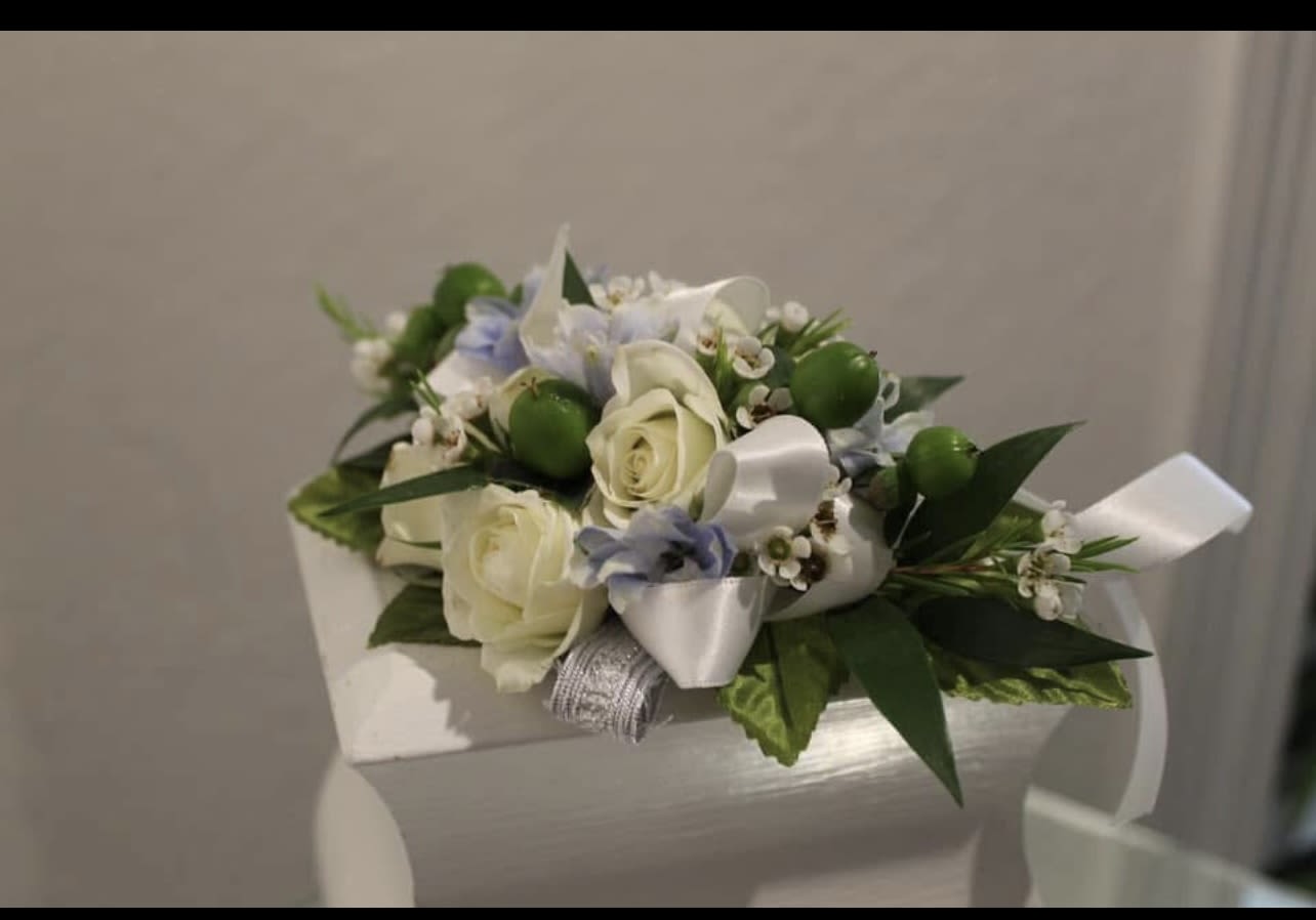 Small arrangement of ivory roses with white and pale blue flowers and ribbon on a white box