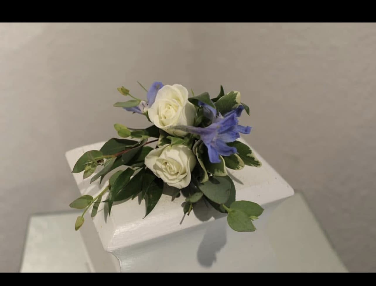Small cluster of white roses and blue flowers arranged on a white pedestal.