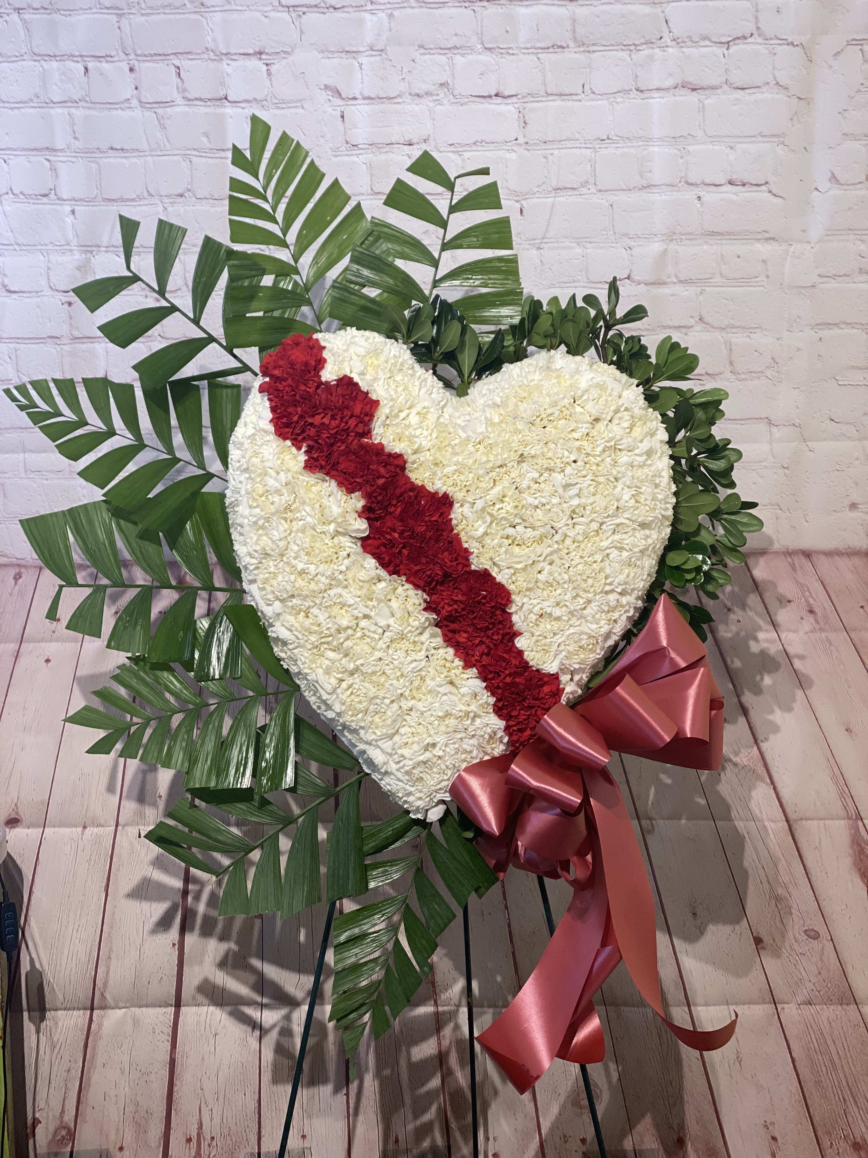Heart-shaped floral tribute with a red diagonal stripe and pink ribbon