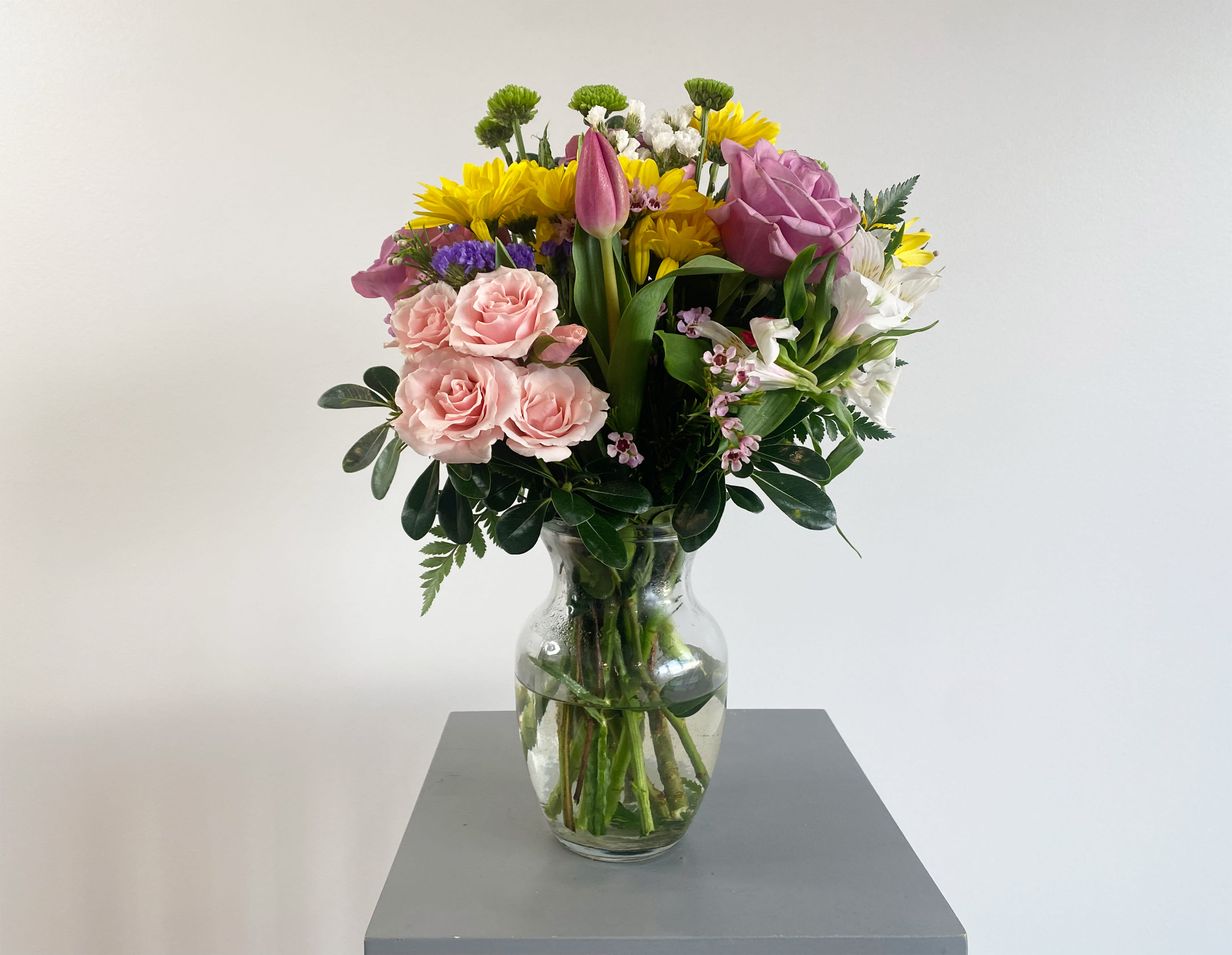 Mixed bouquet of pink roses, yellow daisies, and white flowers in a glass vase