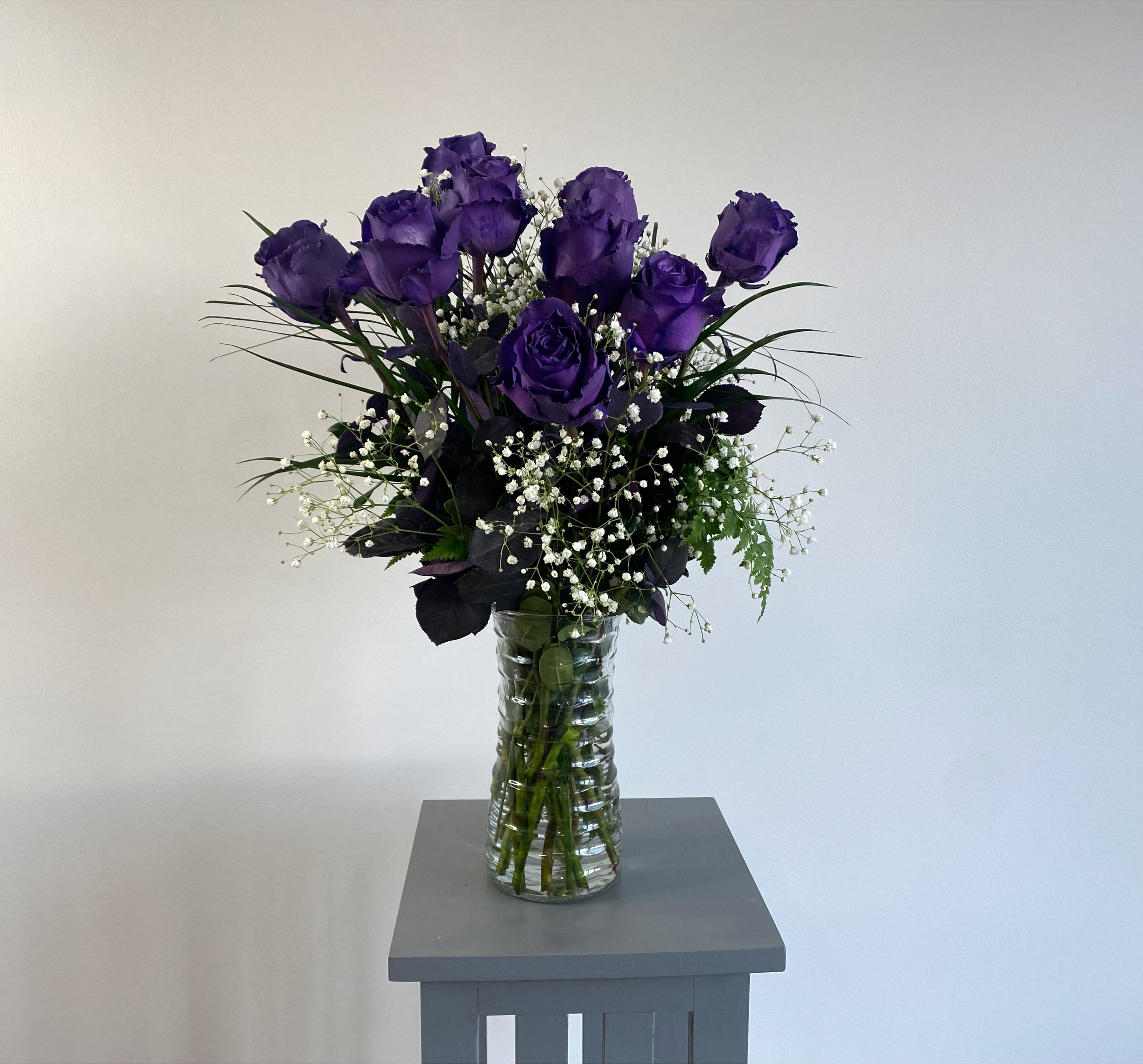 Purple roses in a clear glass vase with white baby's breath