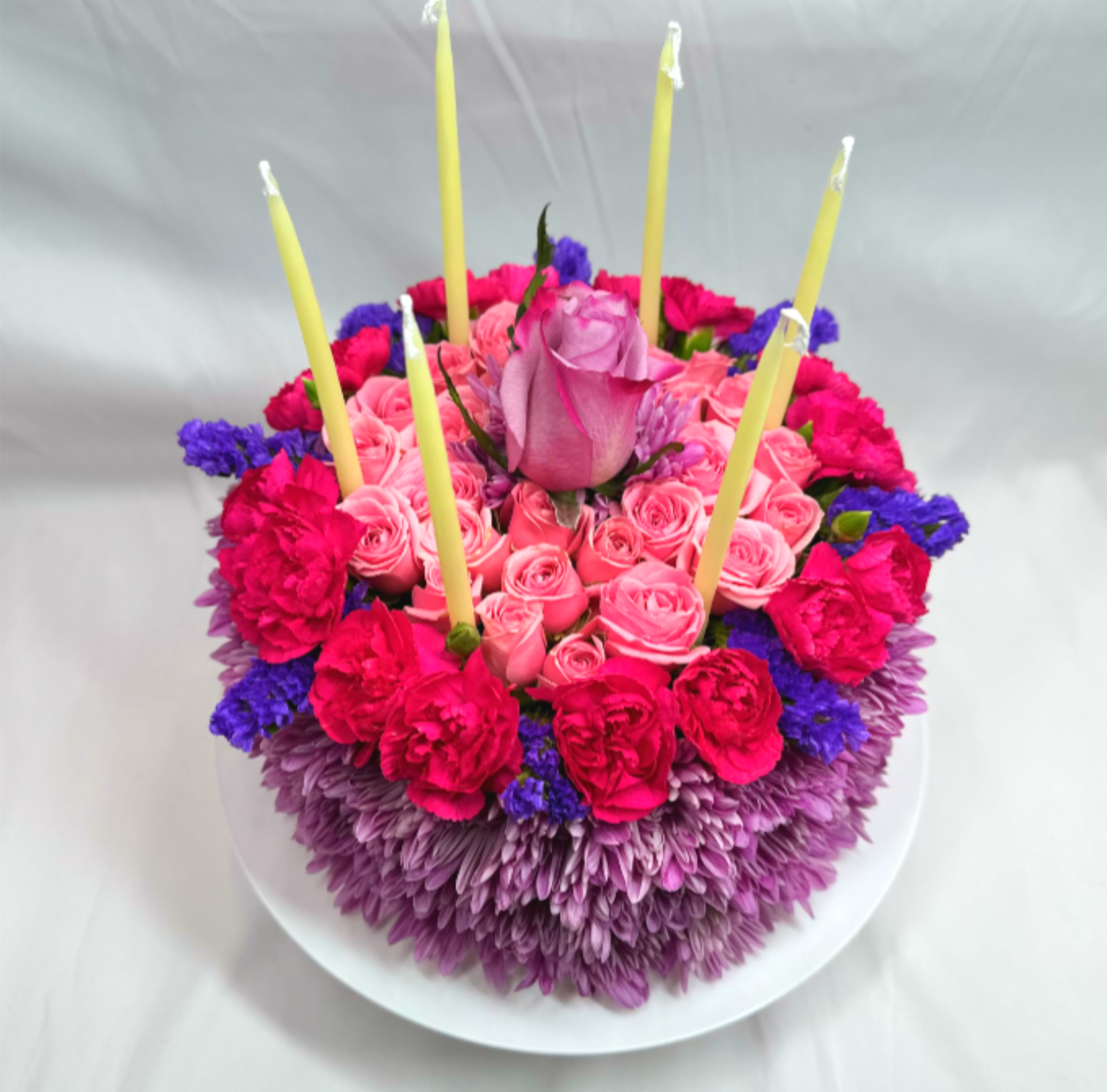 Round floral cake with pink roses and candles on a white plate