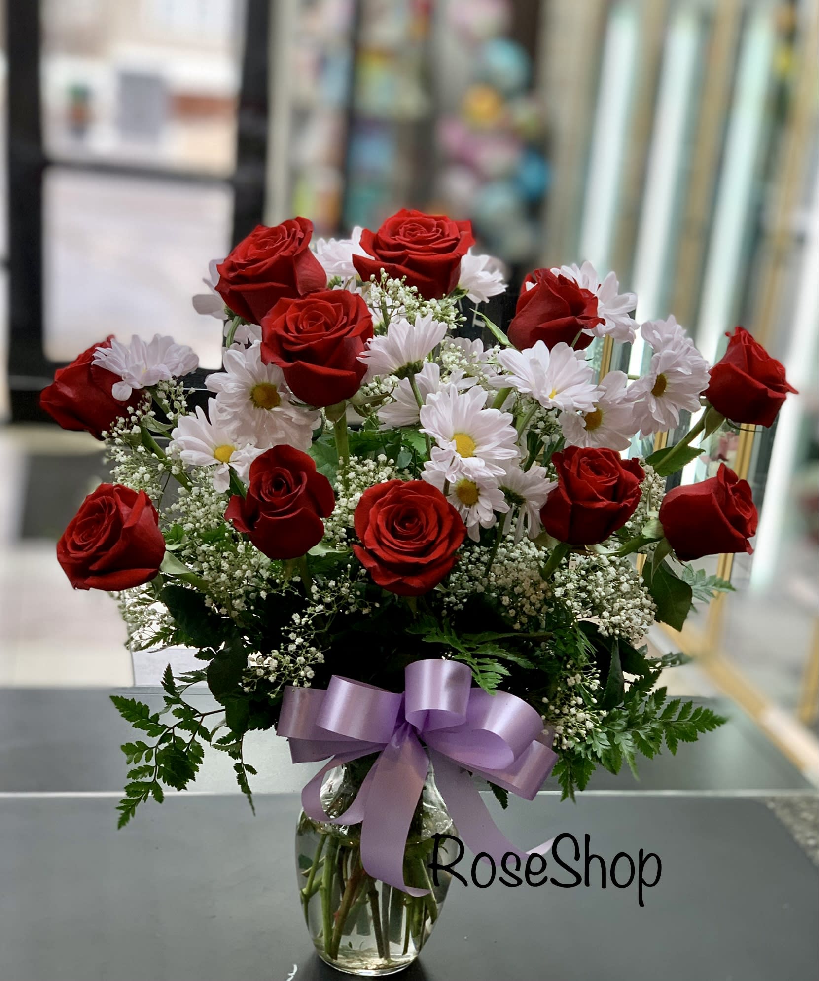 Red roses and white daisies in a glass vase with a lavender ribbon