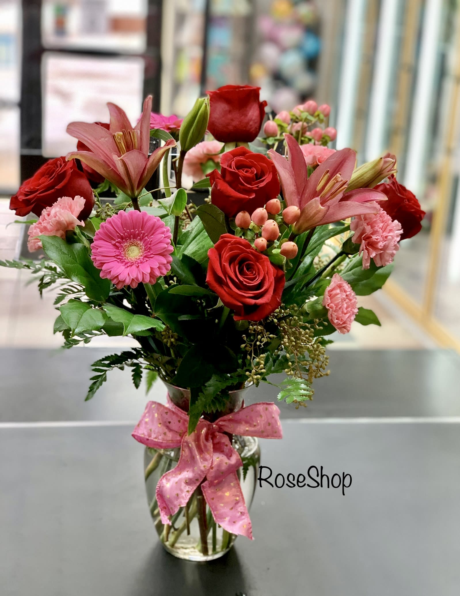 Bouquet of red roses and pink lilies in a glass vase with a pink ribbon