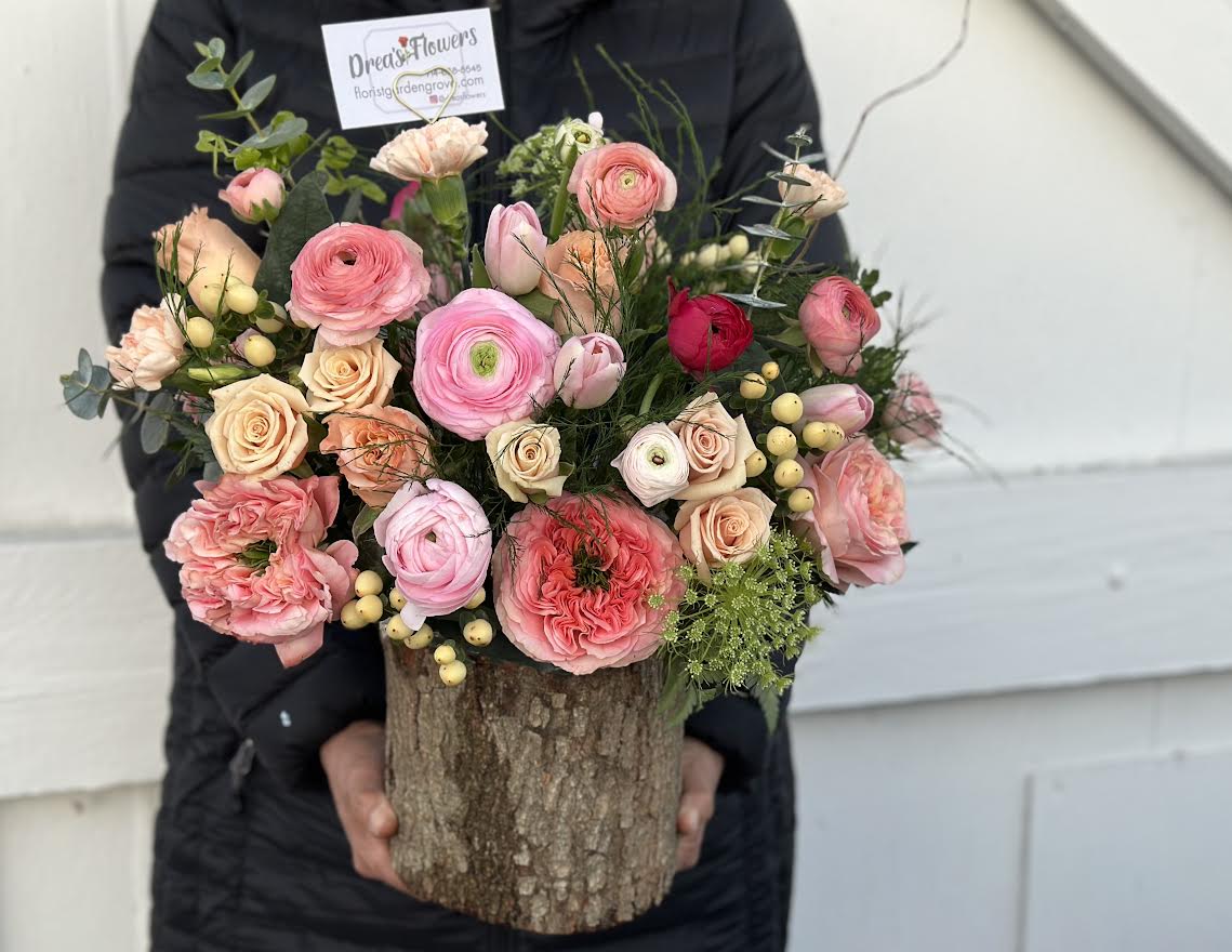 Mixed pink and peach flowers arranged in a rustic wood container