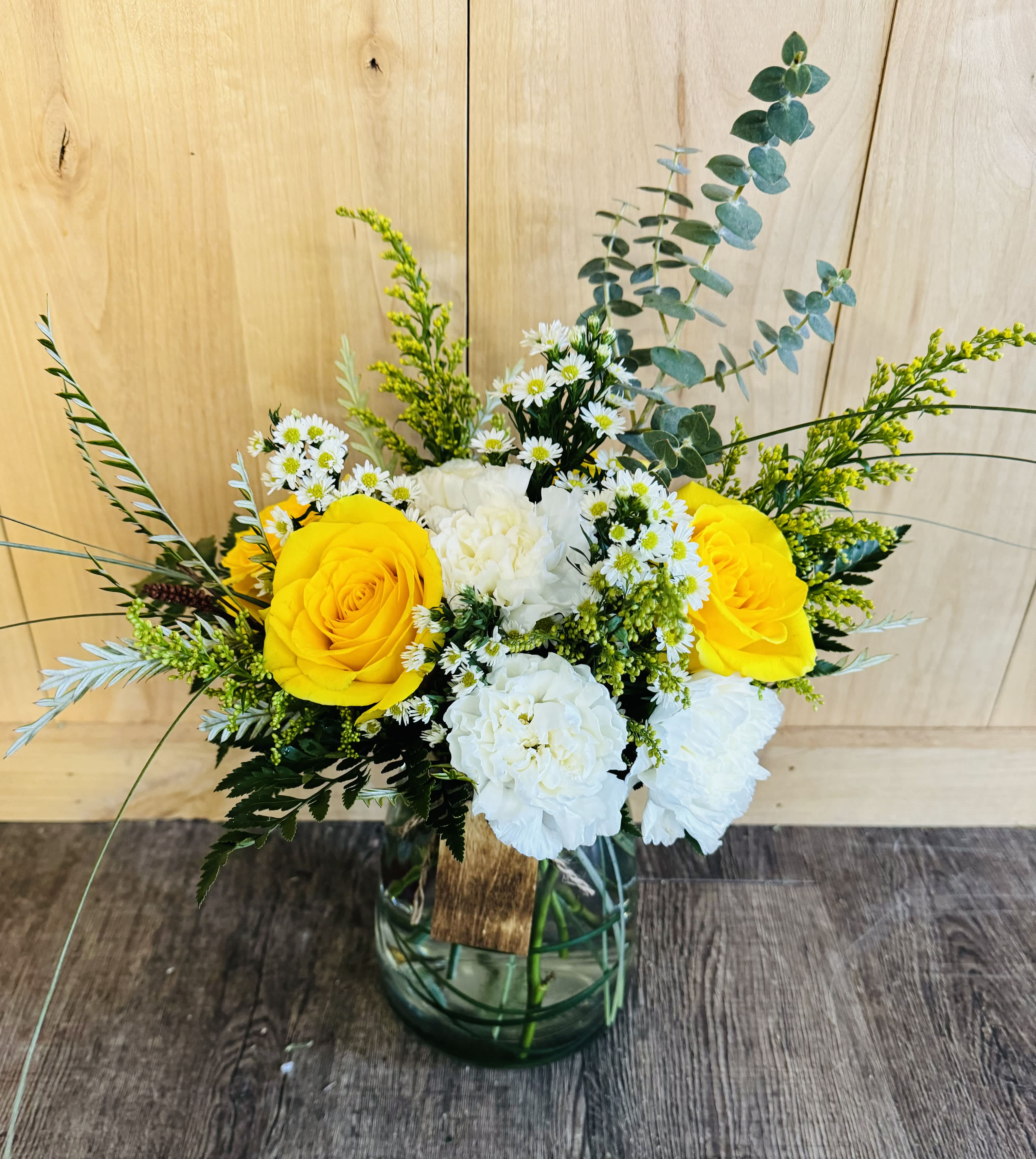 Yellow roses and white flowers in a glass vase with greenery
