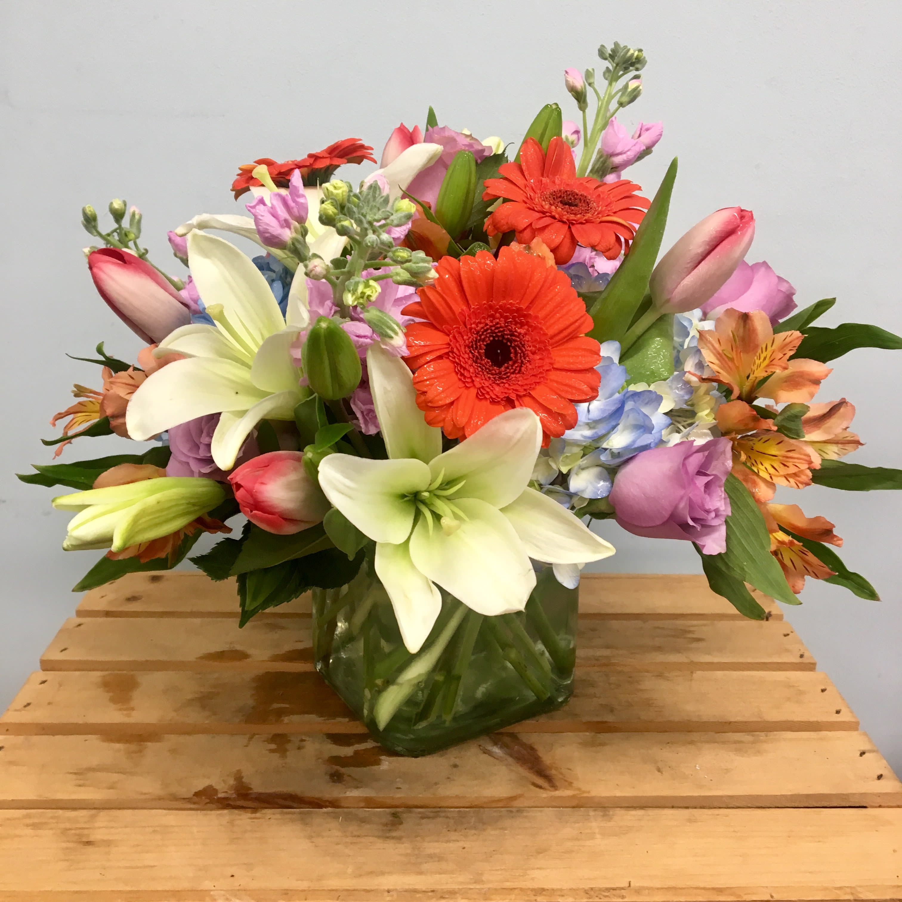 Mixed bouquet with lilies, gerbera daisies, and pastel blooms in a glass vase