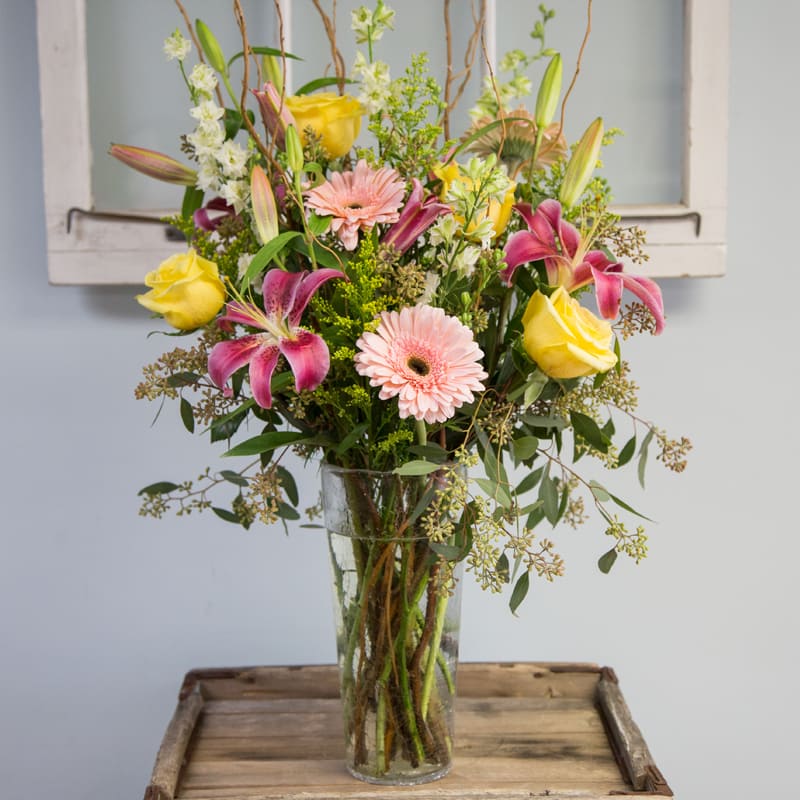 Mixed bouquet of pink lilies, yellow roses, and pale gerbera daisies in a glass vase
