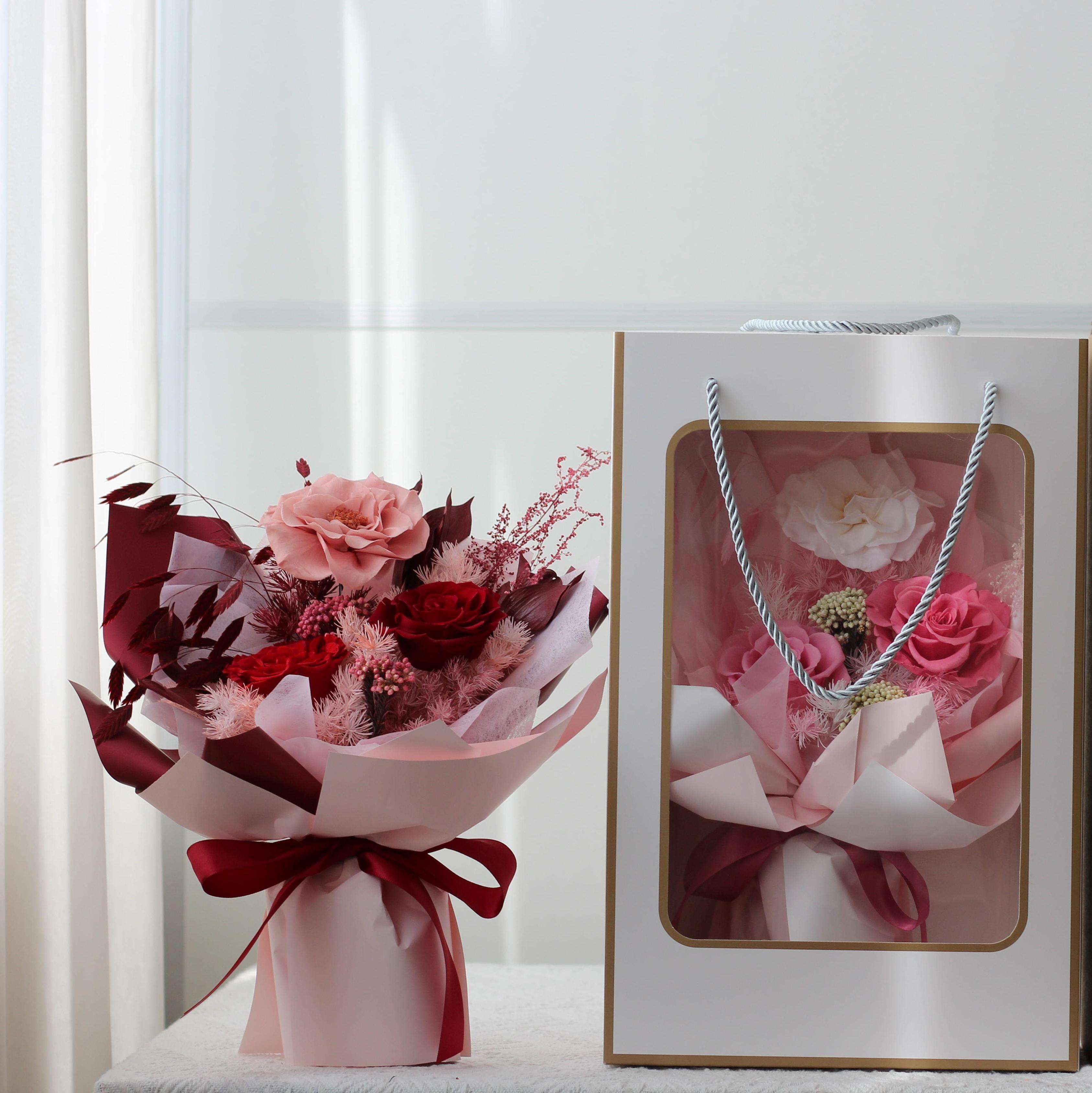 Bouquet of pink and red roses in pink wrapping beside a gift bag