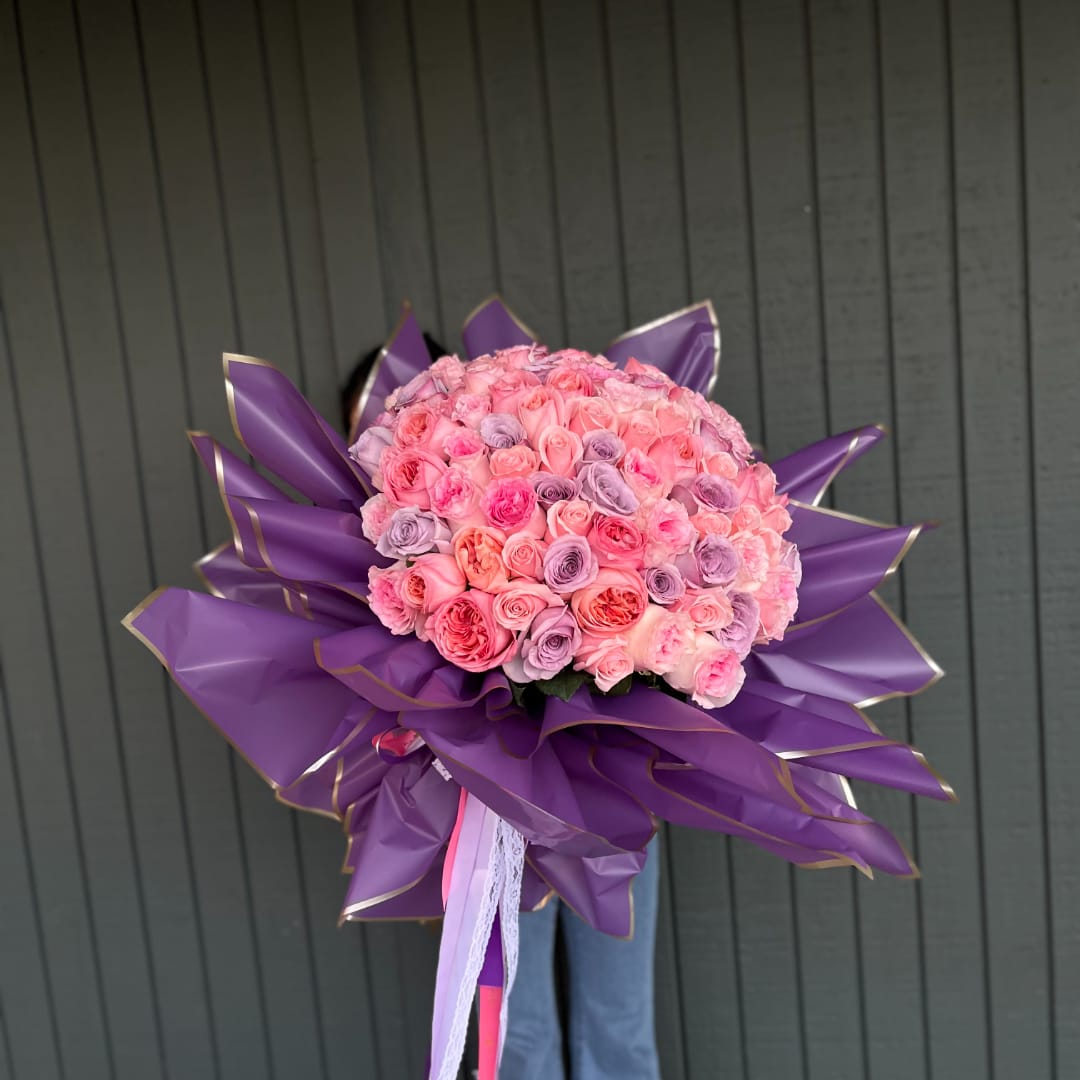 Large bouquet of pink and lavender roses wrapped in purple paper