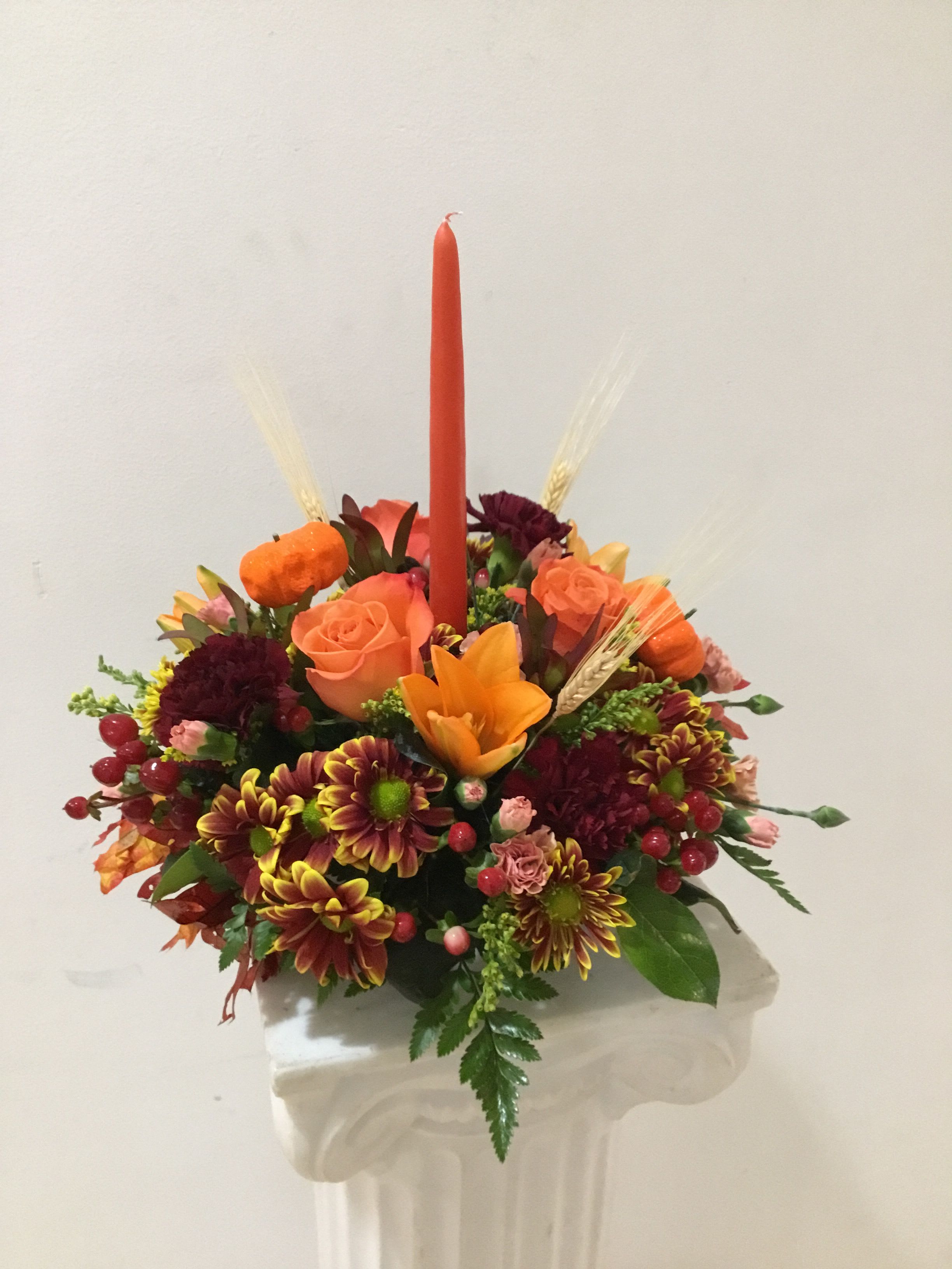 Orange and burgundy floral arrangement with a tall red candle