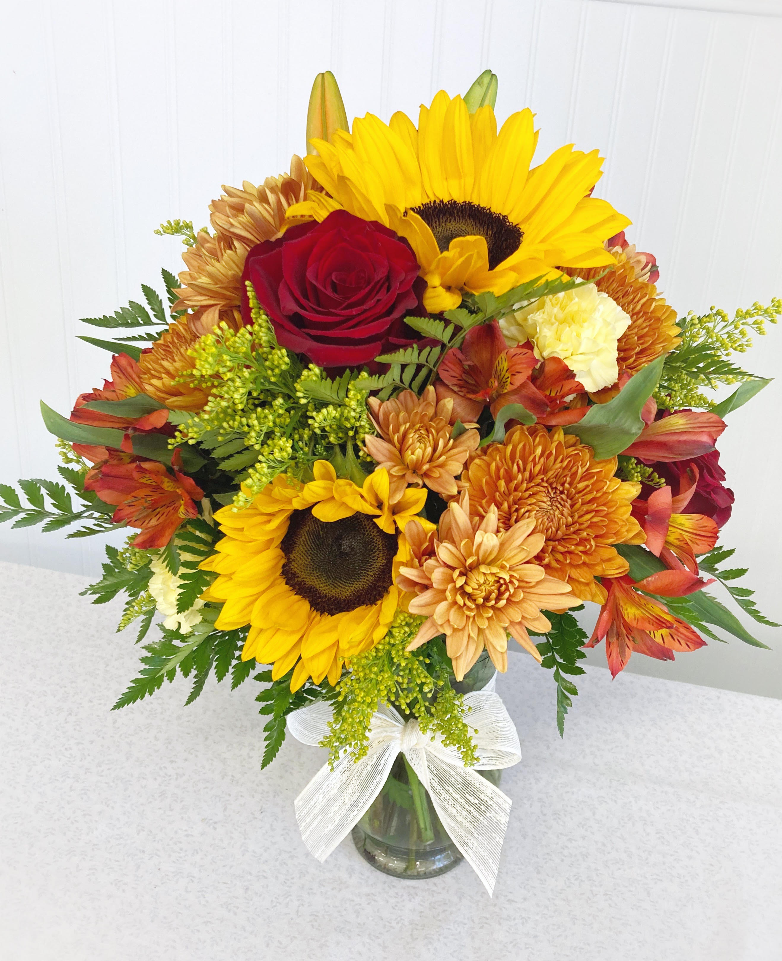 Mixed bouquet with sunflowers, red roses, and orange mums in a glass vase