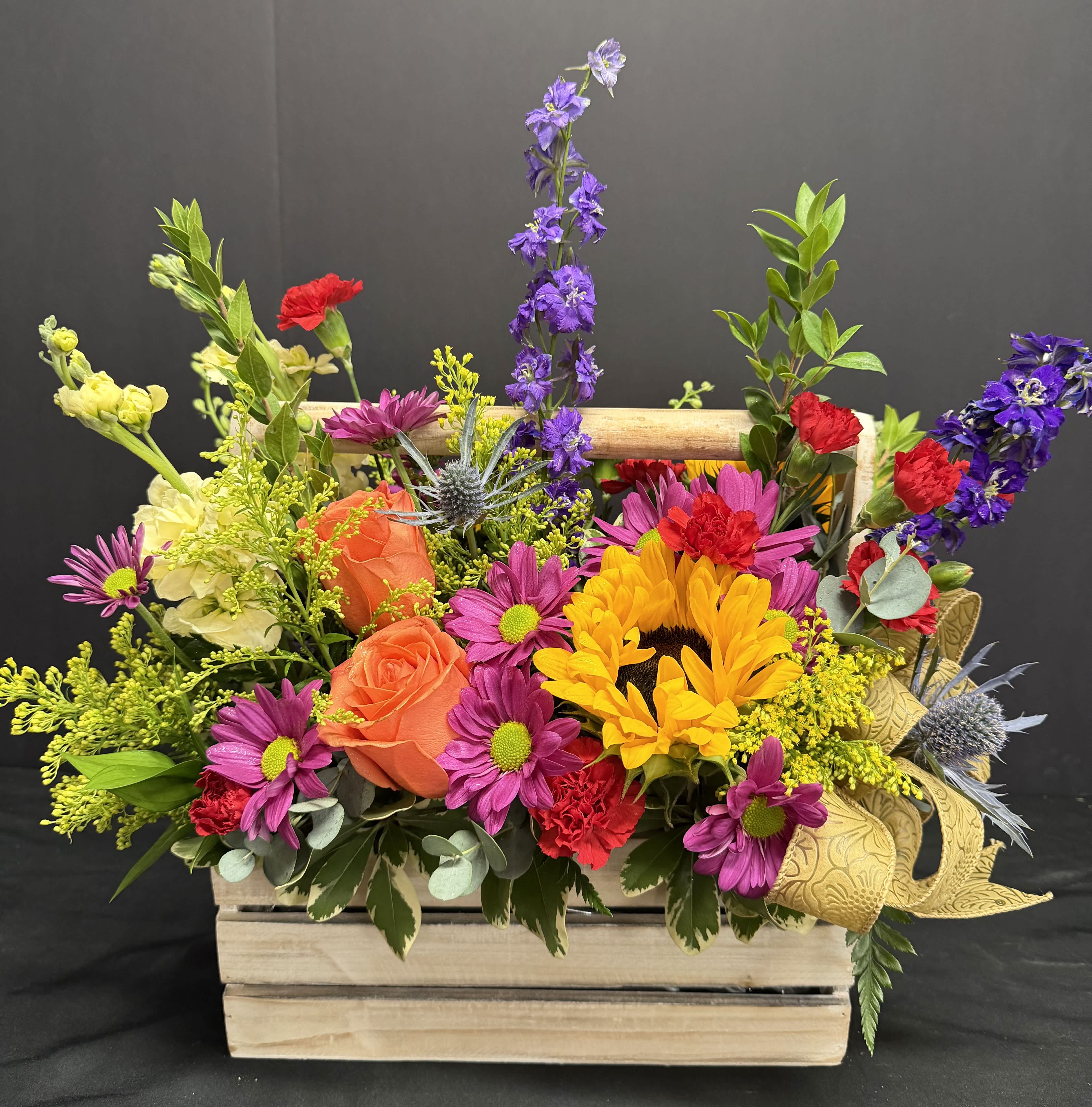 Mixed bouquet in a wooden crate with sunflowers, roses, and purple blooms
