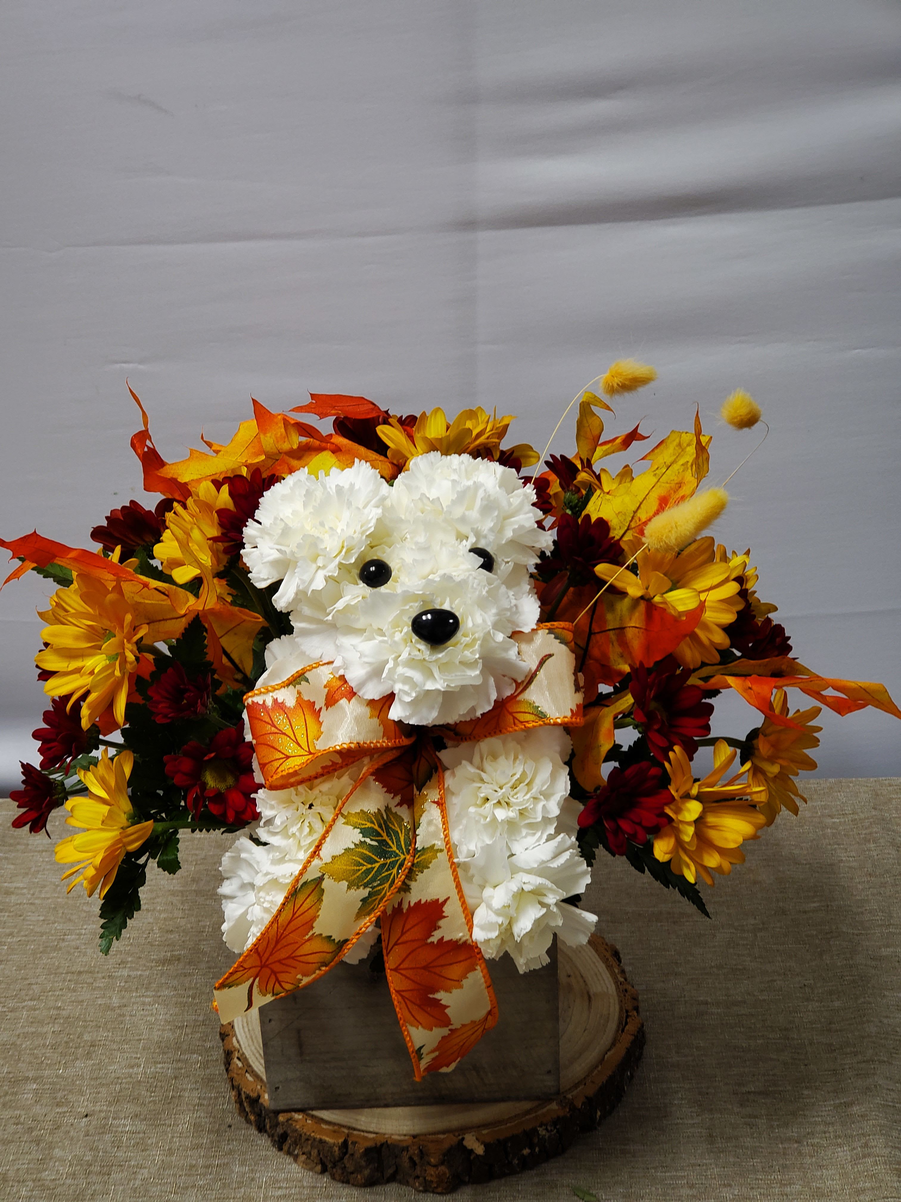 White teddy bear arrangement with autumn flowers and a leaf ribbon in a wooden base