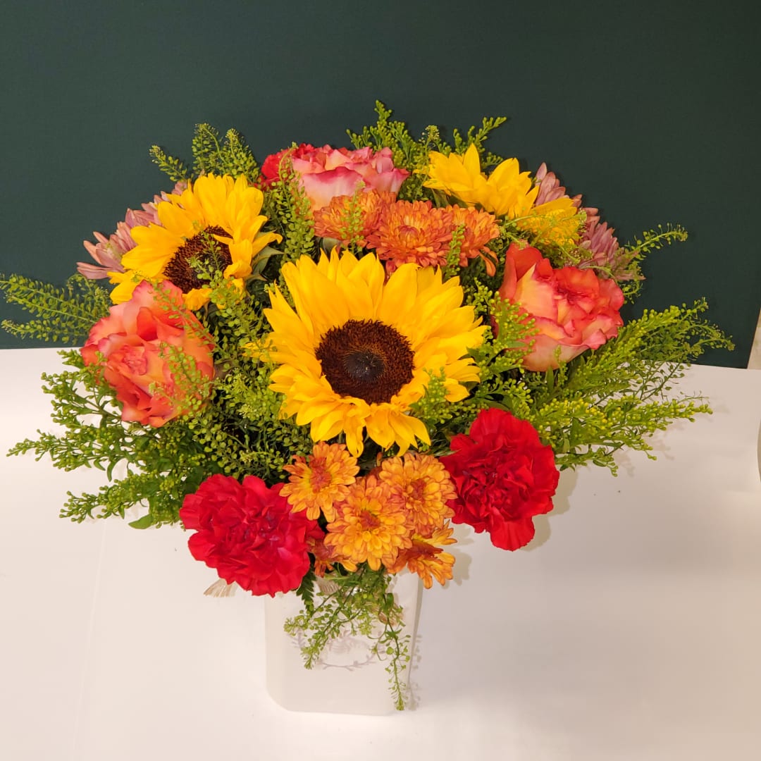 Bright mixed bouquet with sunflowers, roses, and carnations in a white vase