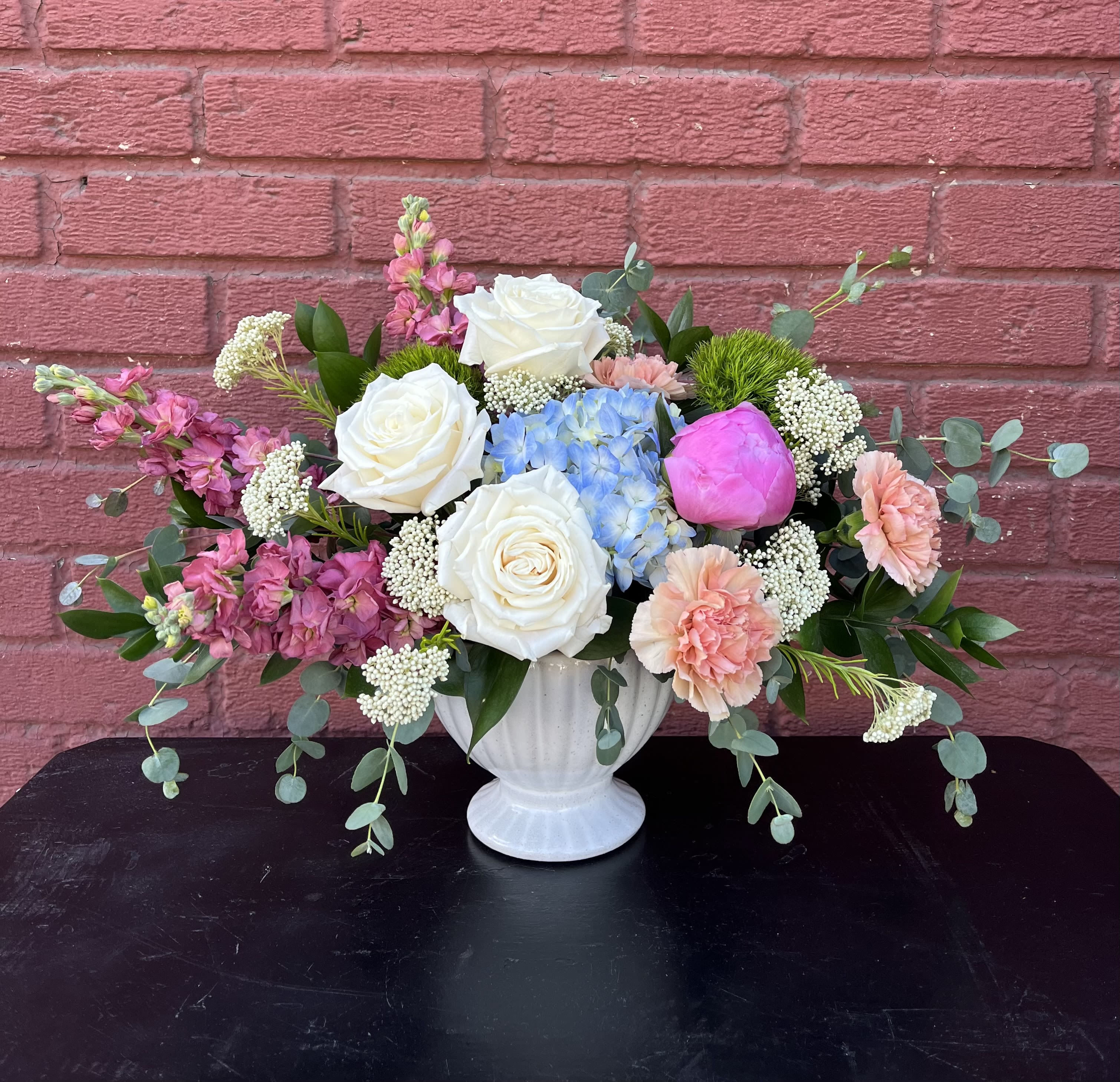 Mixed bouquet in a white vase with white roses, blue hydrangea, and pink blooms