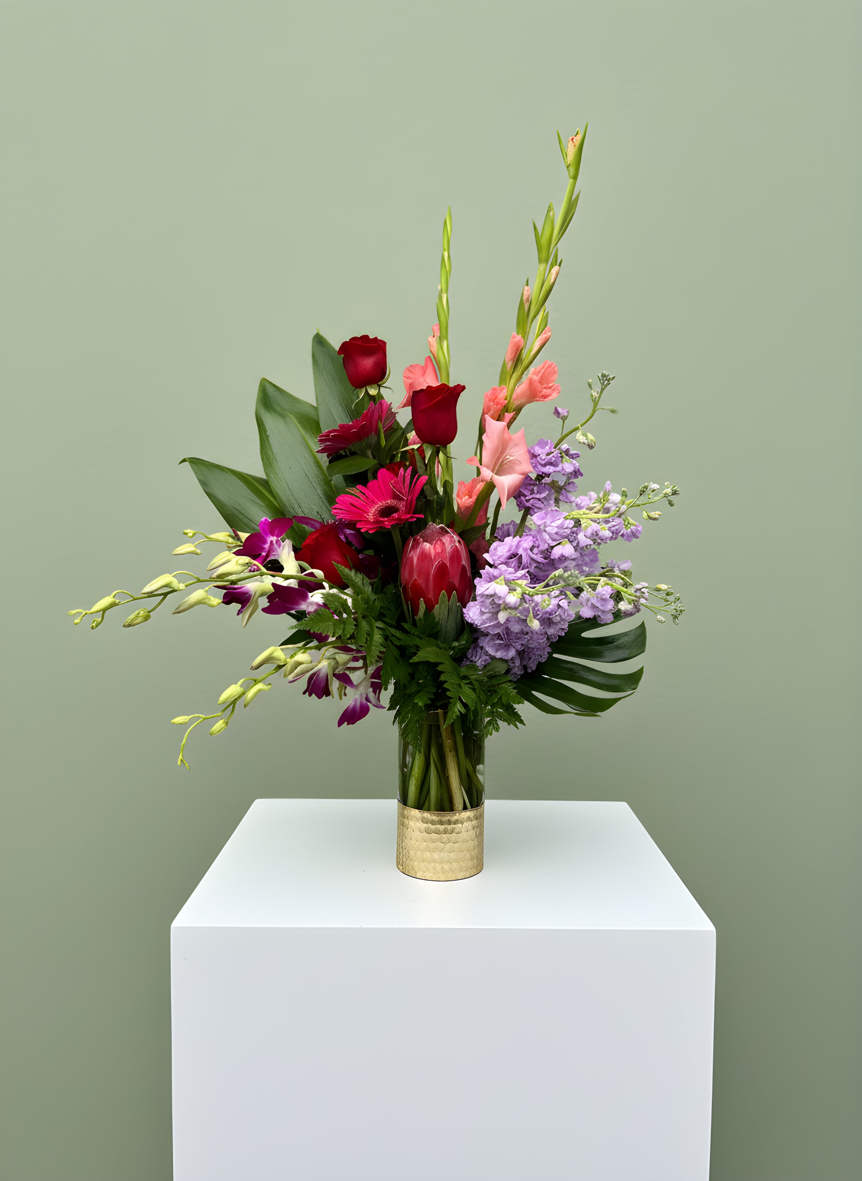 Tropical Luxe Garden - Bold, modern, and effortlessly elegant, our Tropical Luxe Garden arrangement is designed to make a lasting impression. Featuring a striking blend of roses, orchids, gladiolus, stock, and exotic tropical blooms, this design is full of texture, movement, and vibrant color.  Artfully arranged in a sleek gold-accented vase, this piece combines lush greenery with unique focal flowers to create a fresh, contemporary look with a luxurious feel. The mix of soft and bold tones makes it perfect for birthdays, celebrations, or anyone who loves something a little different and eye-catching.  Each arrangement is thoughtfully handcrafted by our floral designers, ensuring every piece is one-of-a-kind and created with care.  Available for same-day flower delivery in Rancho Cucamonga and throughout the Inland Empire, this modern tropical arrangement is a beautiful way to send something truly unforgettable. *Flower varieties may vary based on seasonal availability while maintaining the overall style and color palette.
