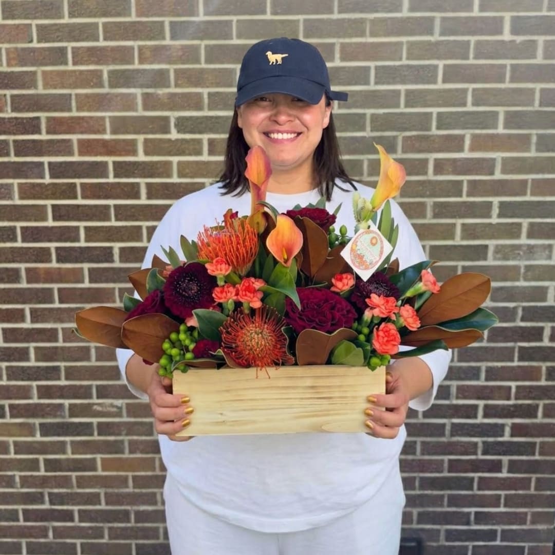 Woman holding a colorful flower arrangement in a wooden box