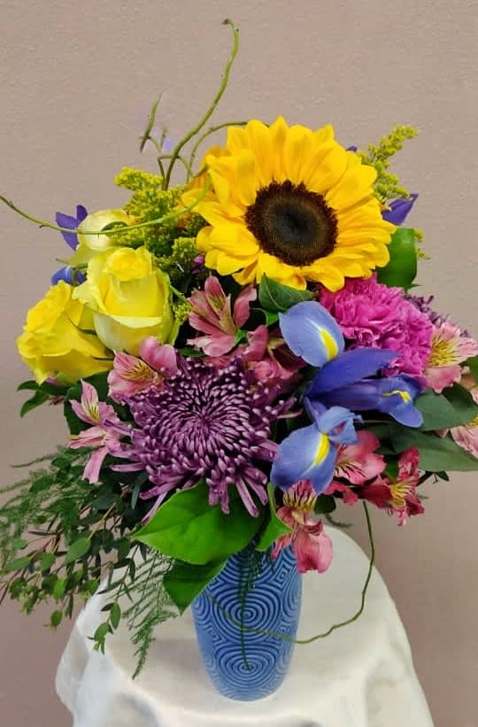 Colorful bouquet with sunflower, roses, and purple blooms in a blue vase